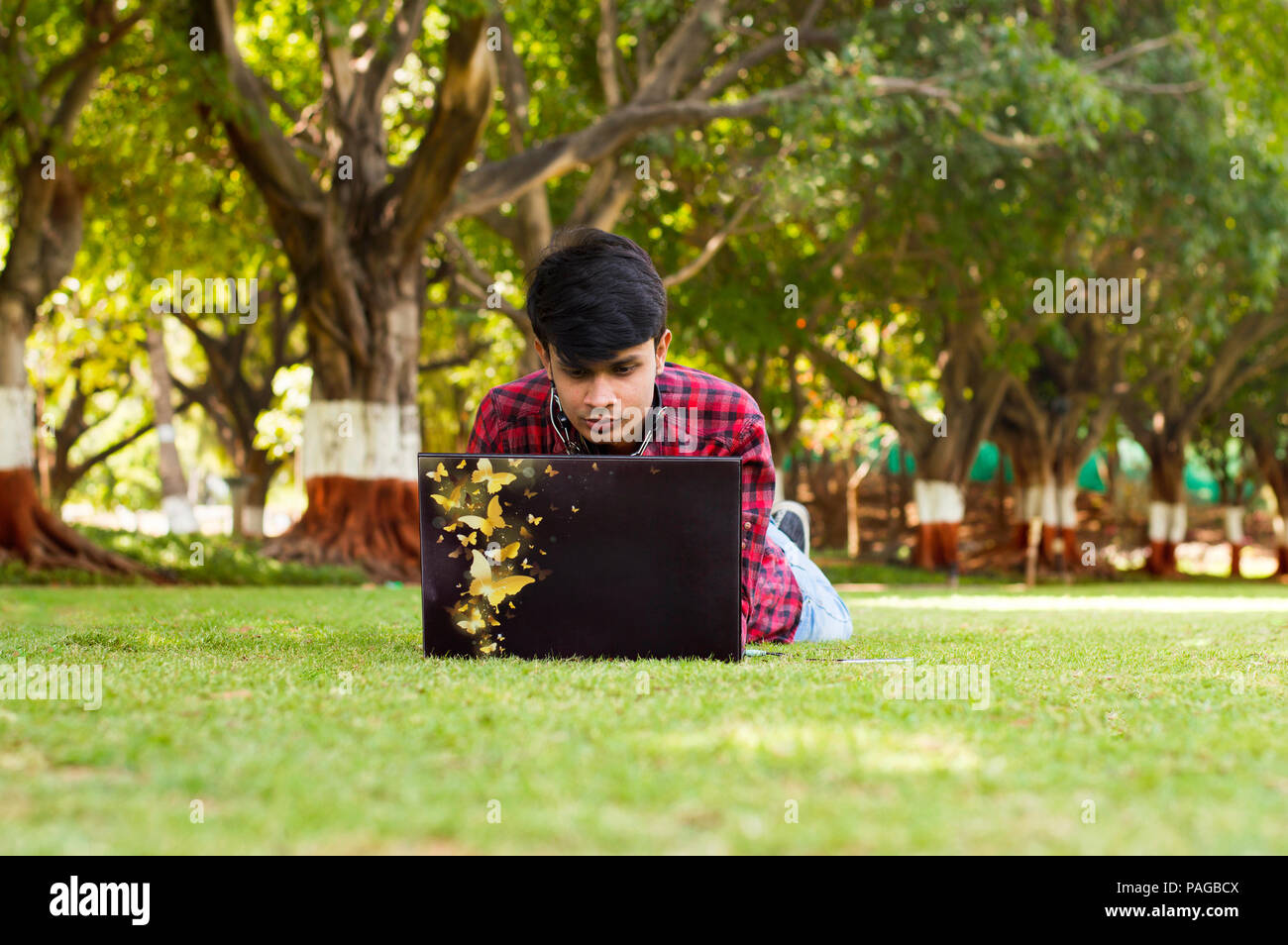 Young handsome student laying on grass and using laptop Stock Photo