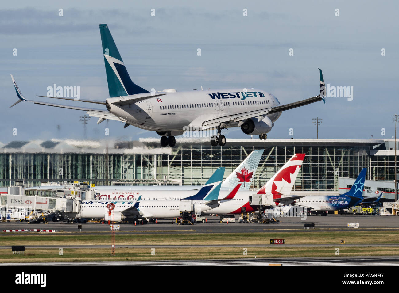Richmond, British Columbia, Canada. 8th July, 2018. A WestJet Airlines Boeing 737-800 (C-FBWI) single-aisle narrow-body jet airliner lands at Vancouver International Airport. In the background airliners from Canadian air carriers WestJet Airlines, Air Canada Rouge, Air Canada and Air Transat are docked at the airport's U.S and International terminal. Credit: Bayne Stanley/ZUMA Wire/Alamy Live News Stock Photo