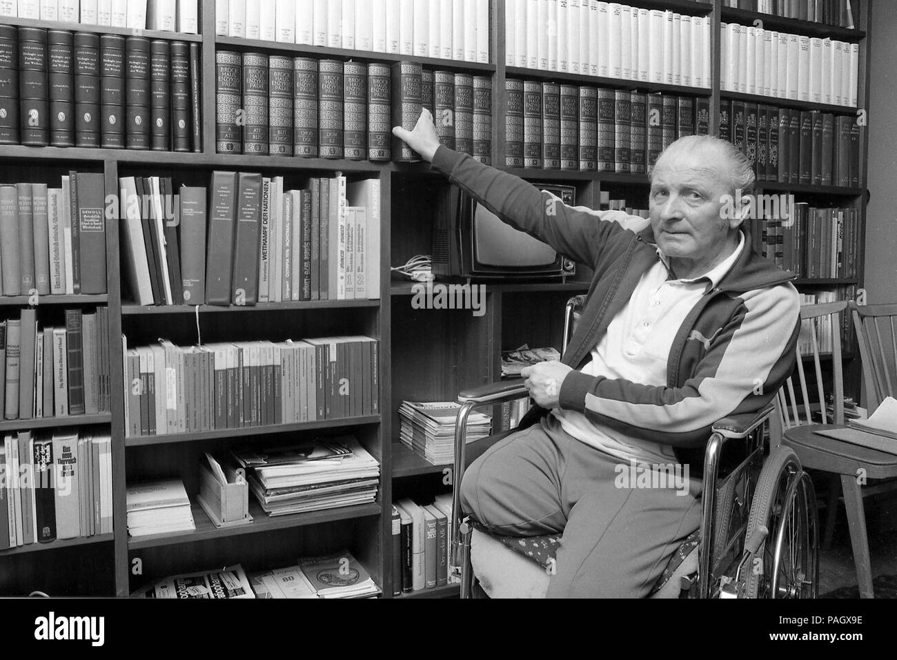 Dr. Ernst Van Aaken sports physician, running coach, private, civil, at home in his living room, library, takes a book from Buecherregal (Bucher shelf), Buecherwand (Bucherwand); In his apartment on 15.04.1980 in Waldniel (Schwalmtal)/Germany; Black and white recording; | usage worldwide Stock Photo