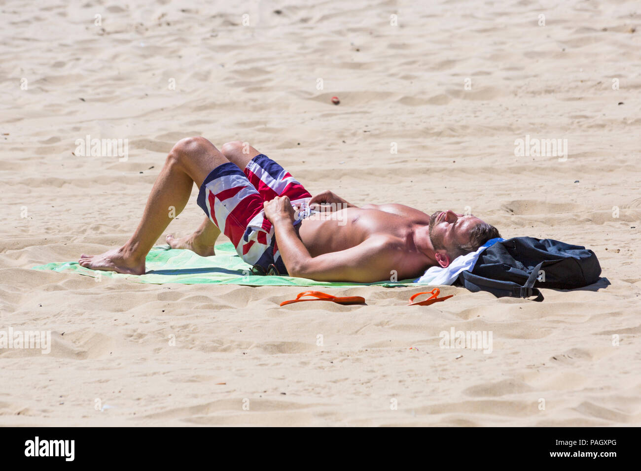 Bournemouth, Dorset, UK. 23rd July 2018. UK weather: the heatwave continues as temperatures rise on a scorching hot and sunny day at Bournemouth beaches with blue skies and unbroken sunshine. Sunseekers head to the seaside to soak up the sun. Man wearing Union Jack shorts sunbathing on beach. Credit: Carolyn Jenkins/Alamy Live News Stock Photo