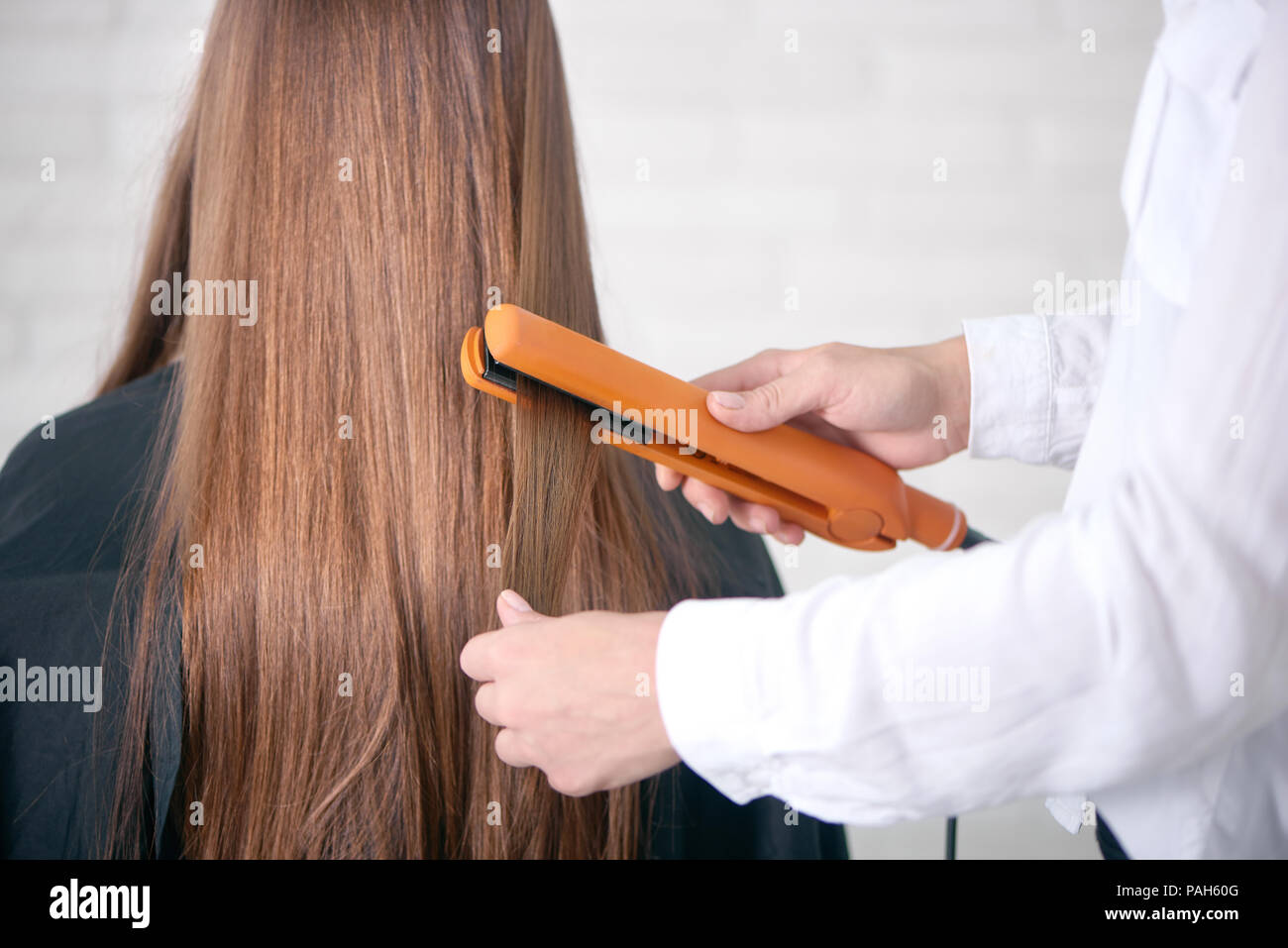 Back view of hairdresser straighting client's long brown hair. Model having  smooth, straight, glancy, healthy hair, sitting covered with special black  cape. Hairstyler wearing white classic shirt Stock Photo - Alamy