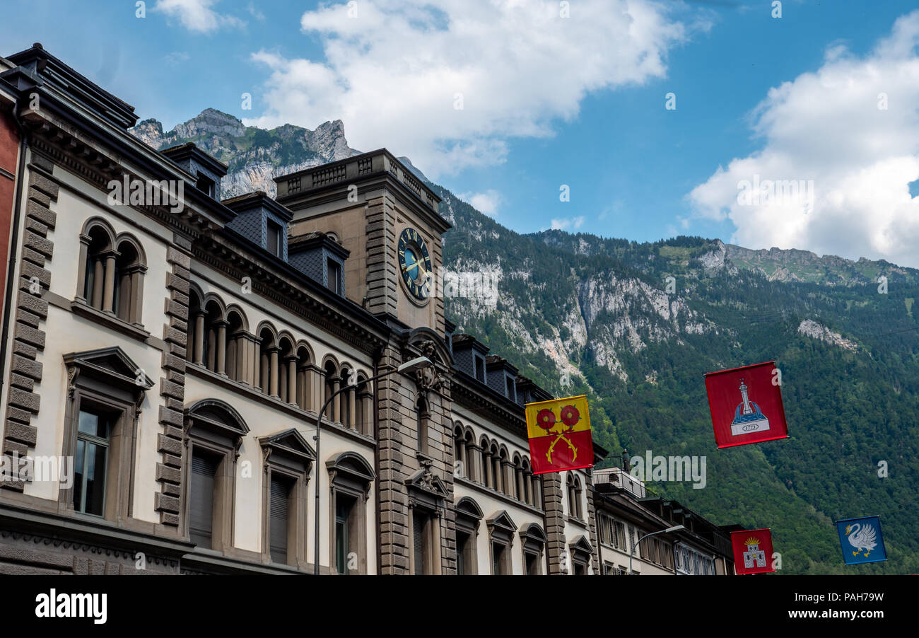 glarus, switzerland. old building with clock and swiss canton flags infront of mountain scenery Stock Photo