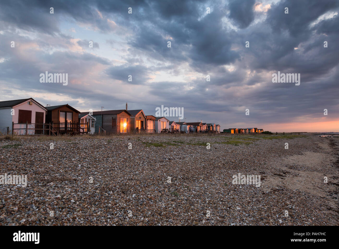 Golden sunset light shining on the beach huts by the shingle beach at Seasalter, Whitstable, Kent, UK. Dramatic clouds are seen above. Stock Photo