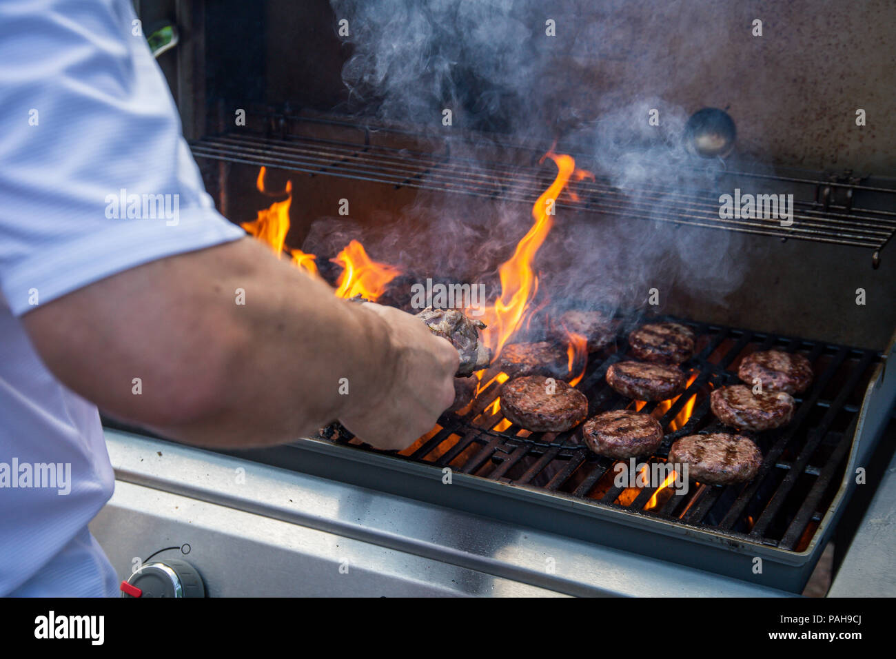 Marinated lamb joint and beef burgers cooking on a barbecue with flames