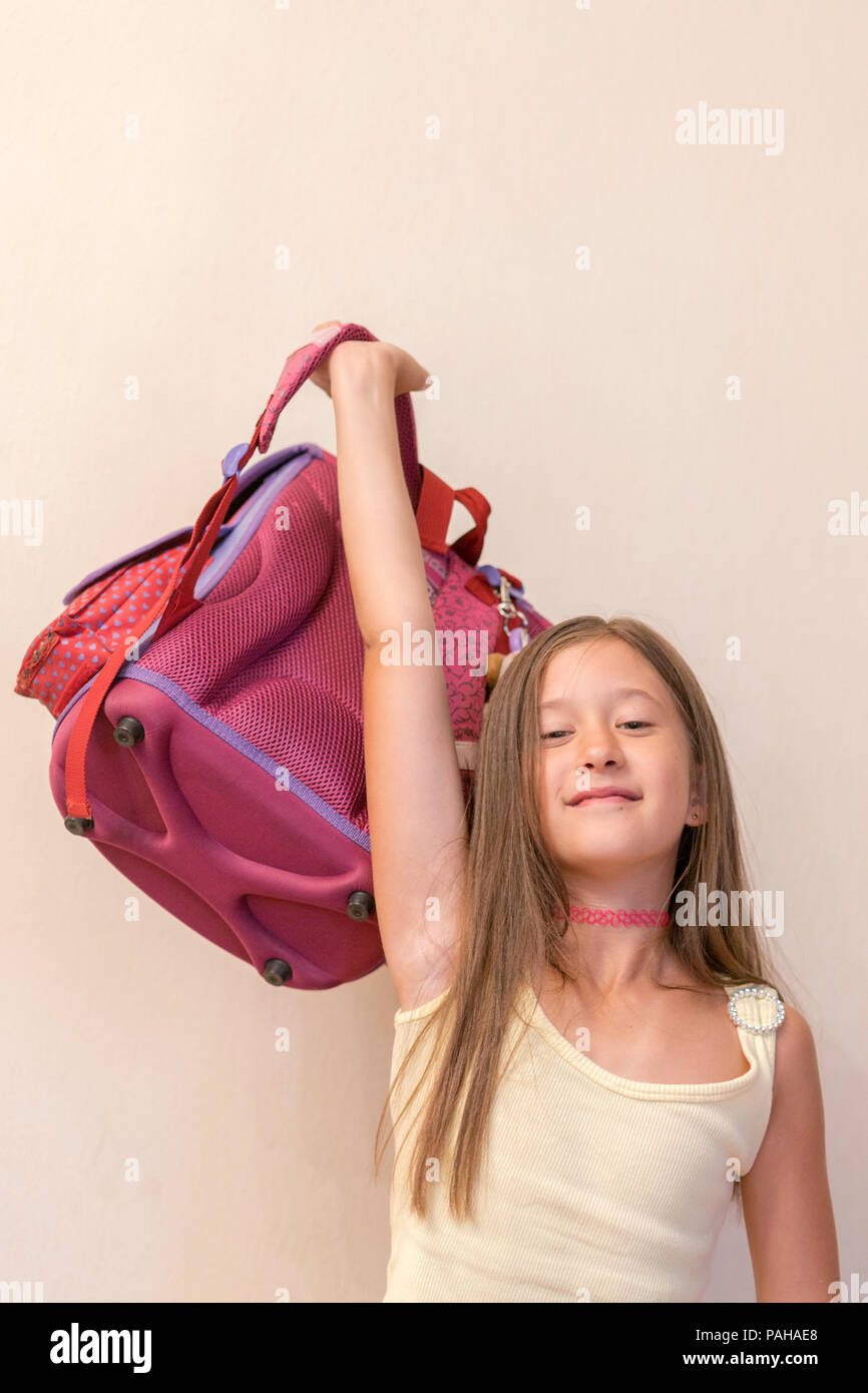 Funny little girl with big backpack jumping and having fun against white wall. School concept. Back to School. School's out for summer. Celebrating th Stock Photo