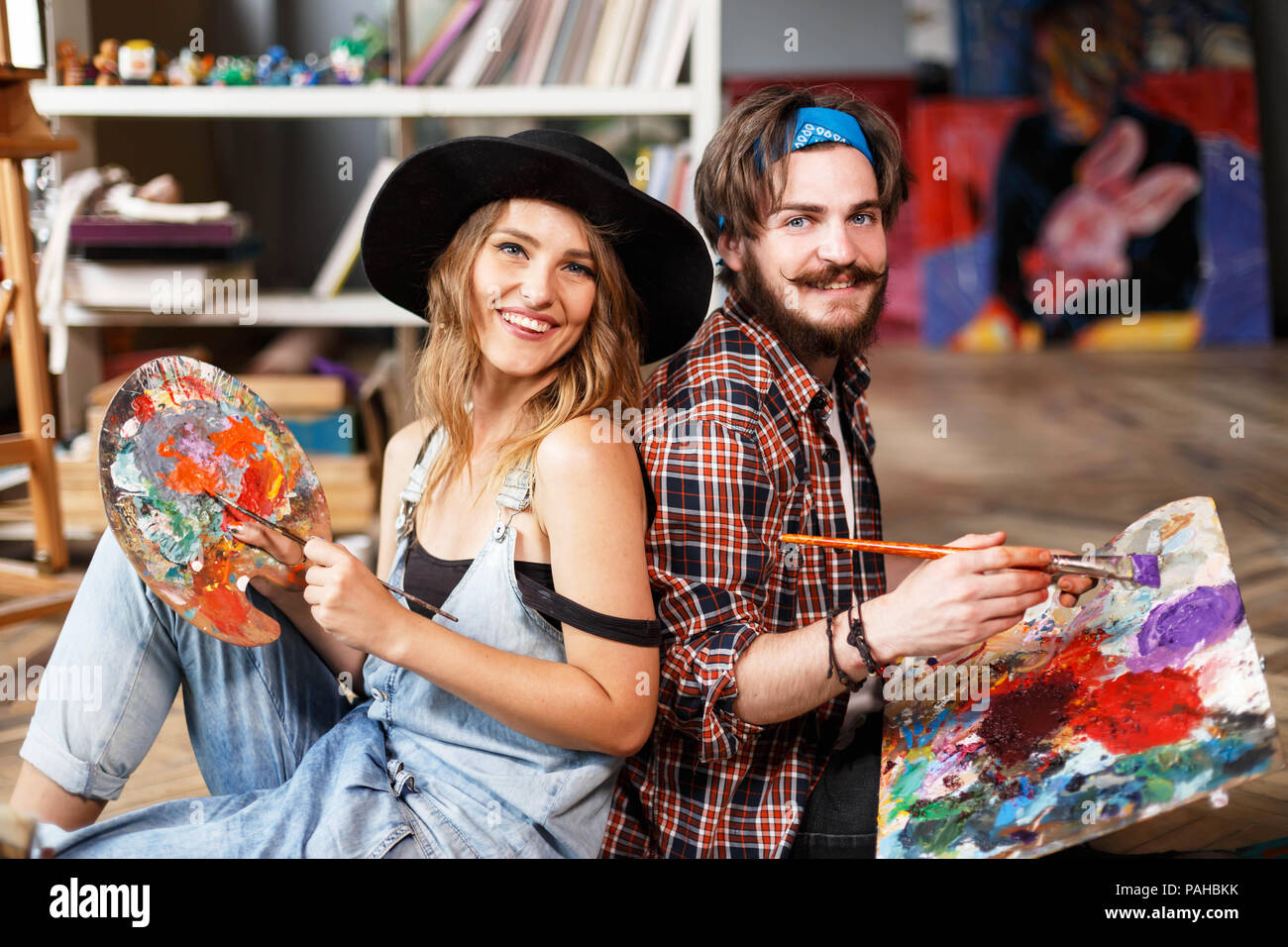 Two pretty smiling artists dressed in hipster clothes holding brushes