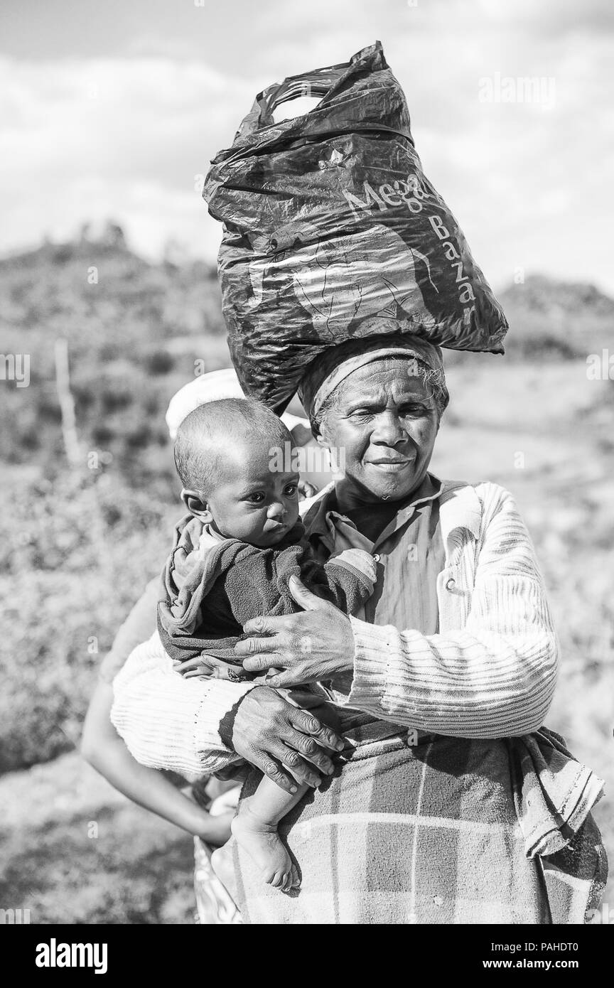 ANTANANARIVO, MADAGASCAR - JUNE 30, 2011: Unidentified Madagascar woman carries her child and some other things the street. People in Madagascar suffe Stock Photo