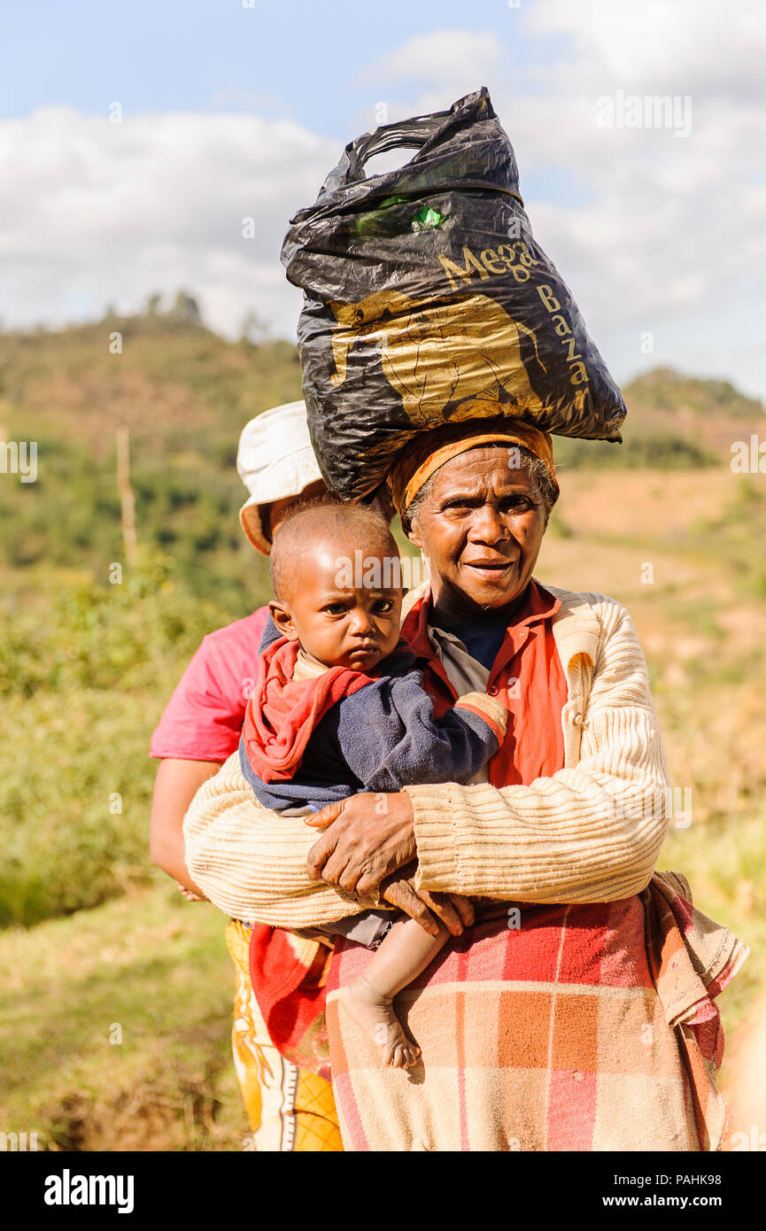 ANTANANARIVO, MADAGASCAR - JUNE 30, 2011: Unidentified Madagascar woman carries her child and some other things the street. People in Madagascar suffe Stock Photo