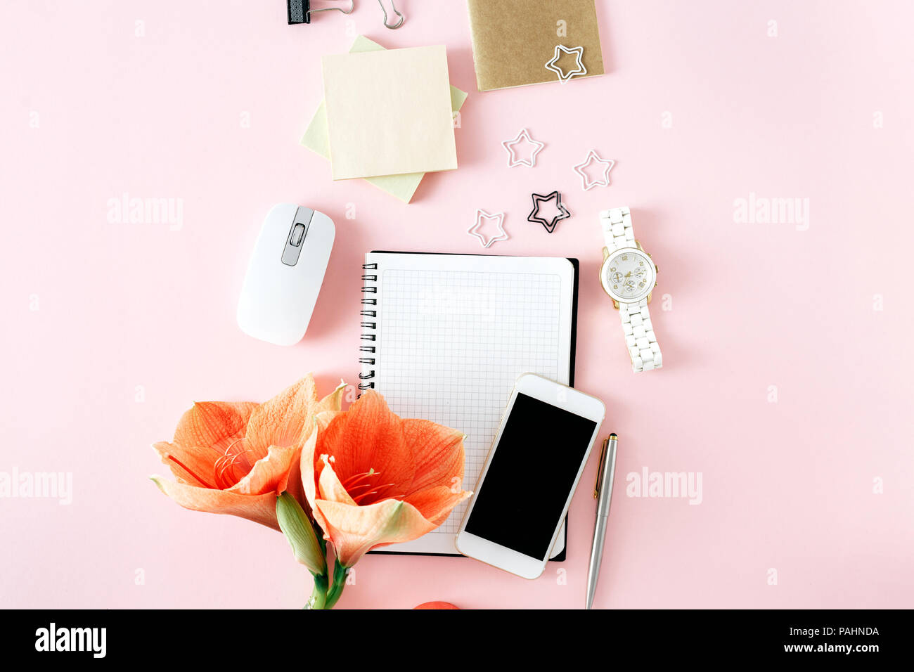 Flat lay, top view office table desk. Feminine desk workspace with flower amaryllis, notebook, pen, smartphone, computer mouse and womens on pink back Stock Photo