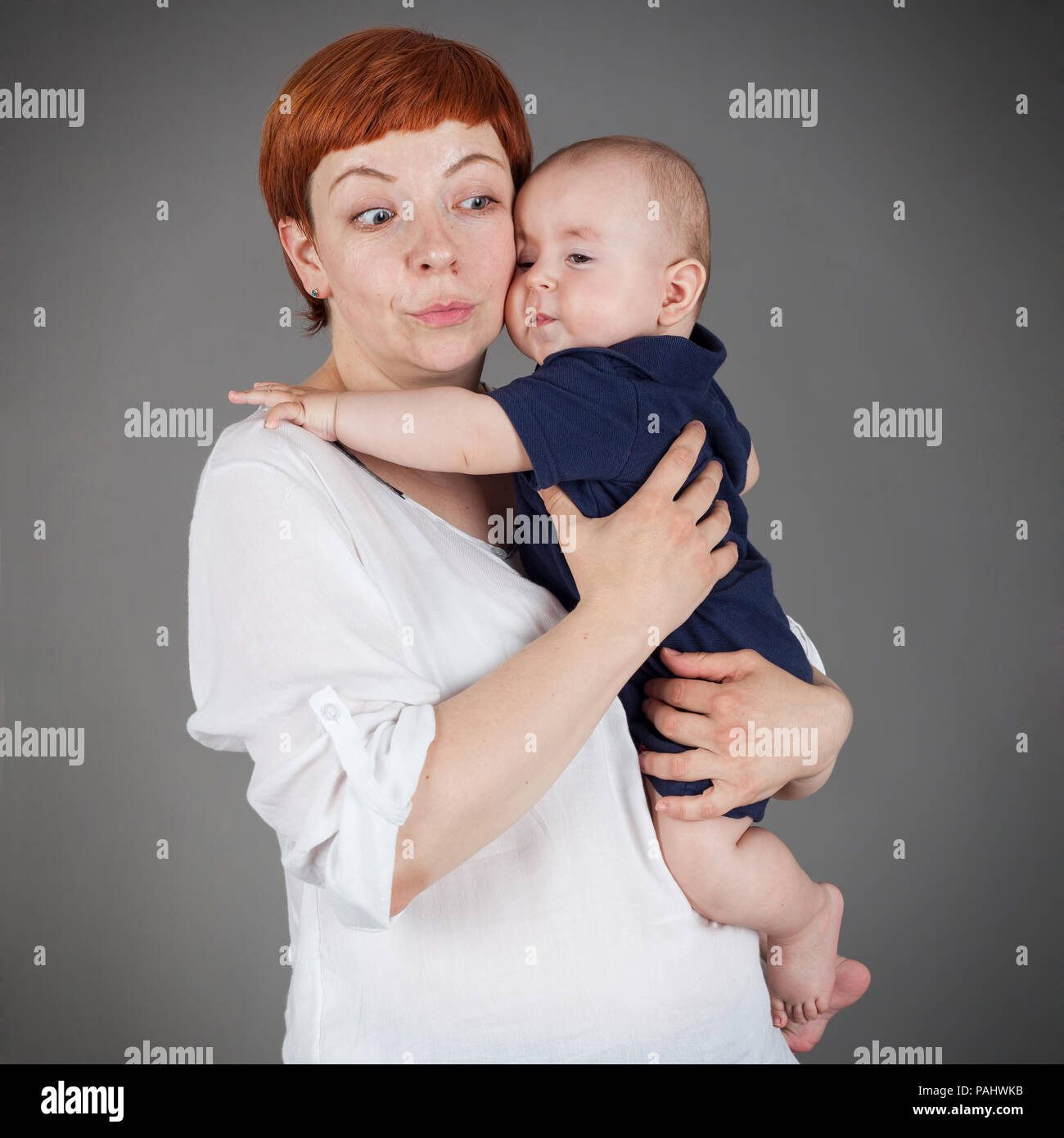 Mother looking surprised towards the lower corner of the frame, holding a baby, square, isolated on grey with vignette Stock Photo