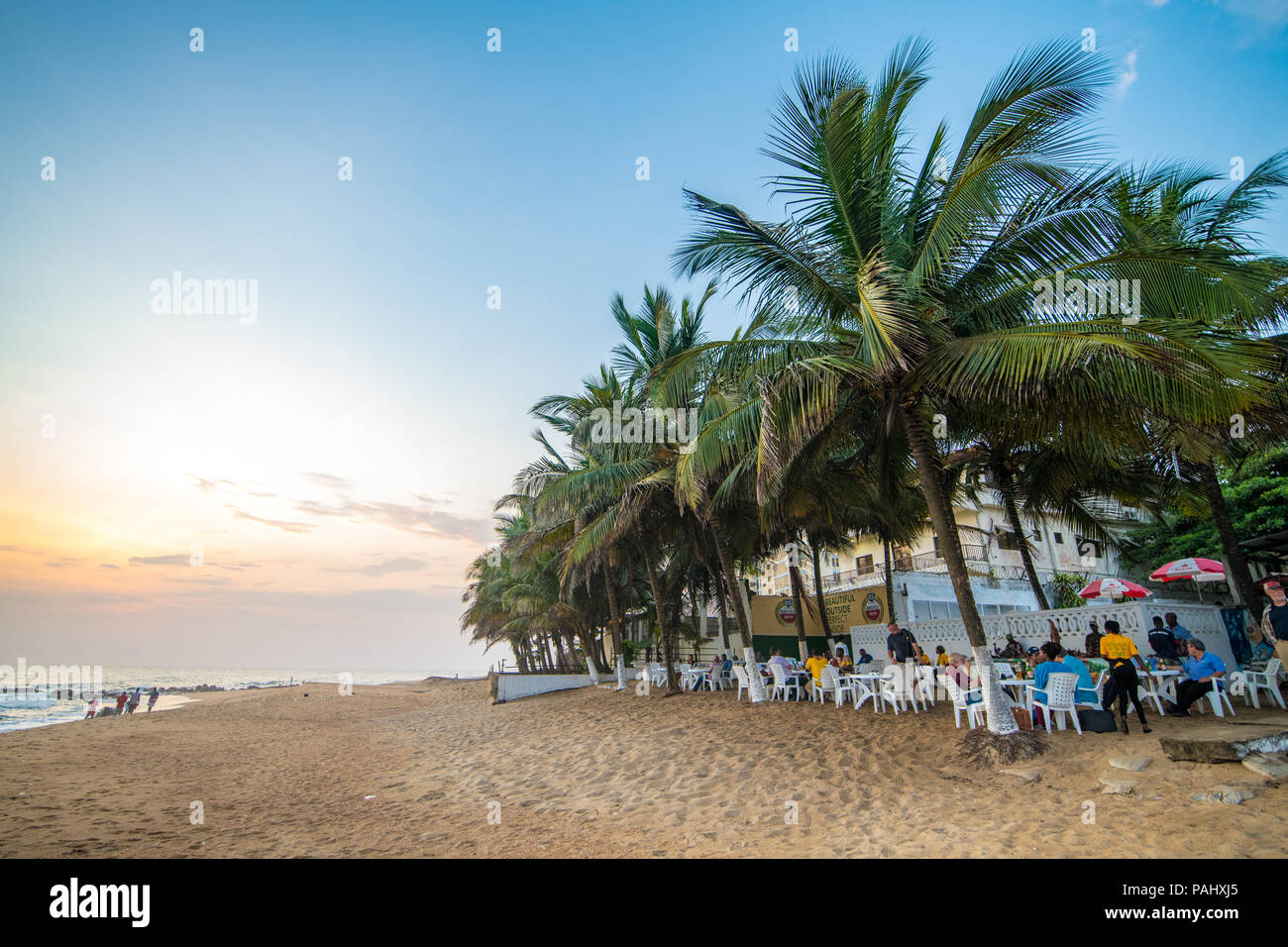 Groups of people are seated at tables along the beach at a restaurant. Monrovia, Liberia Stock Photo
