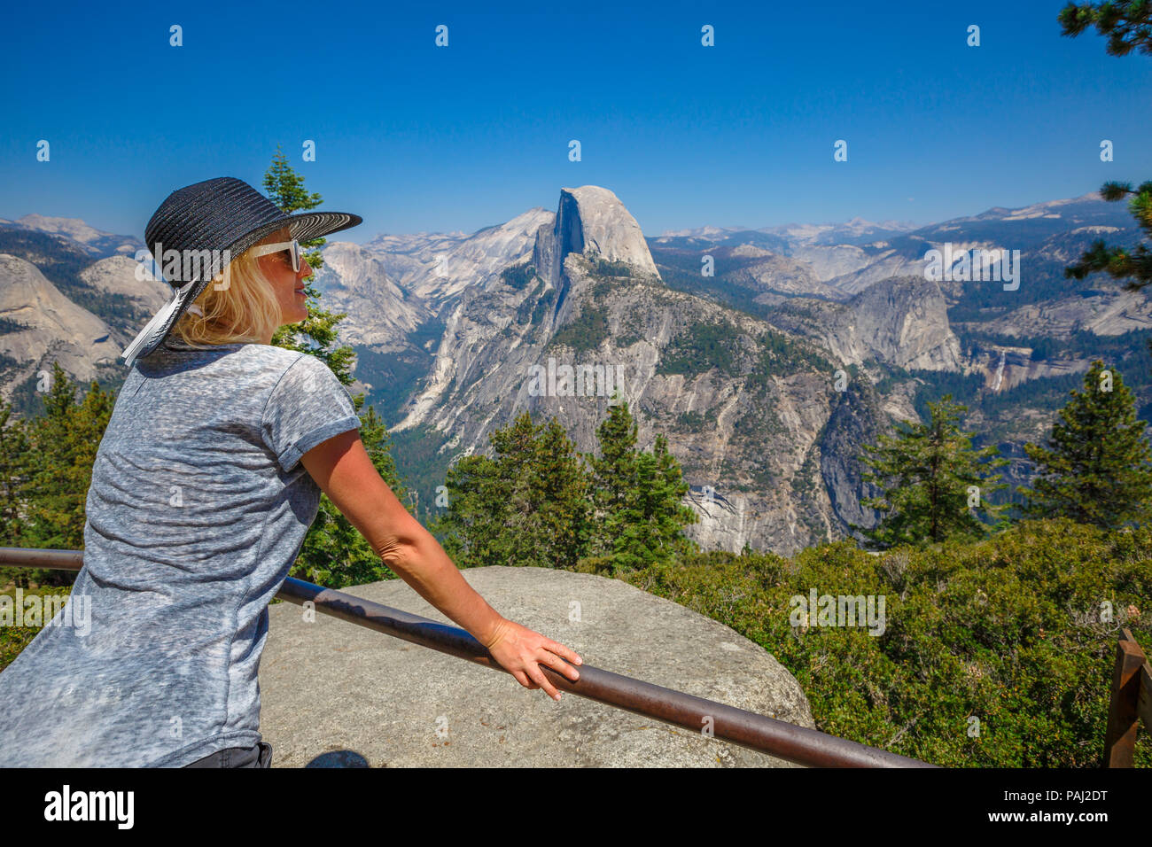 Traveler lifestyle woman with hat contemplating Glacier Point in Yosemite National Park. Relaxing at popular Half Dome from Glacier Point overlook. American travel holidays concept. California, USA. Stock Photo