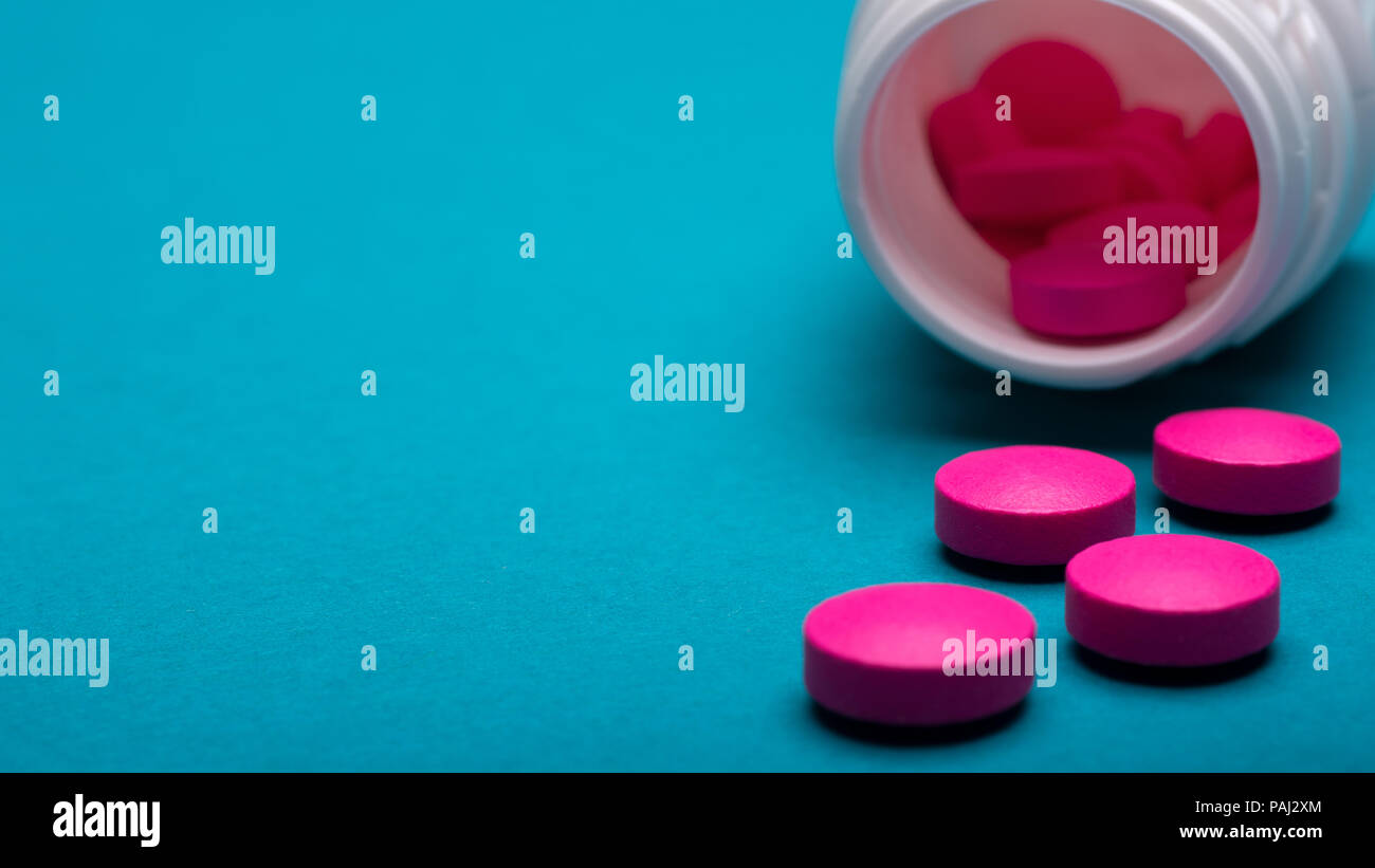 Medication bottle and bright pink pills spilled on dark blue coloured background. Medication and prescription pills close up background. Stock Photo