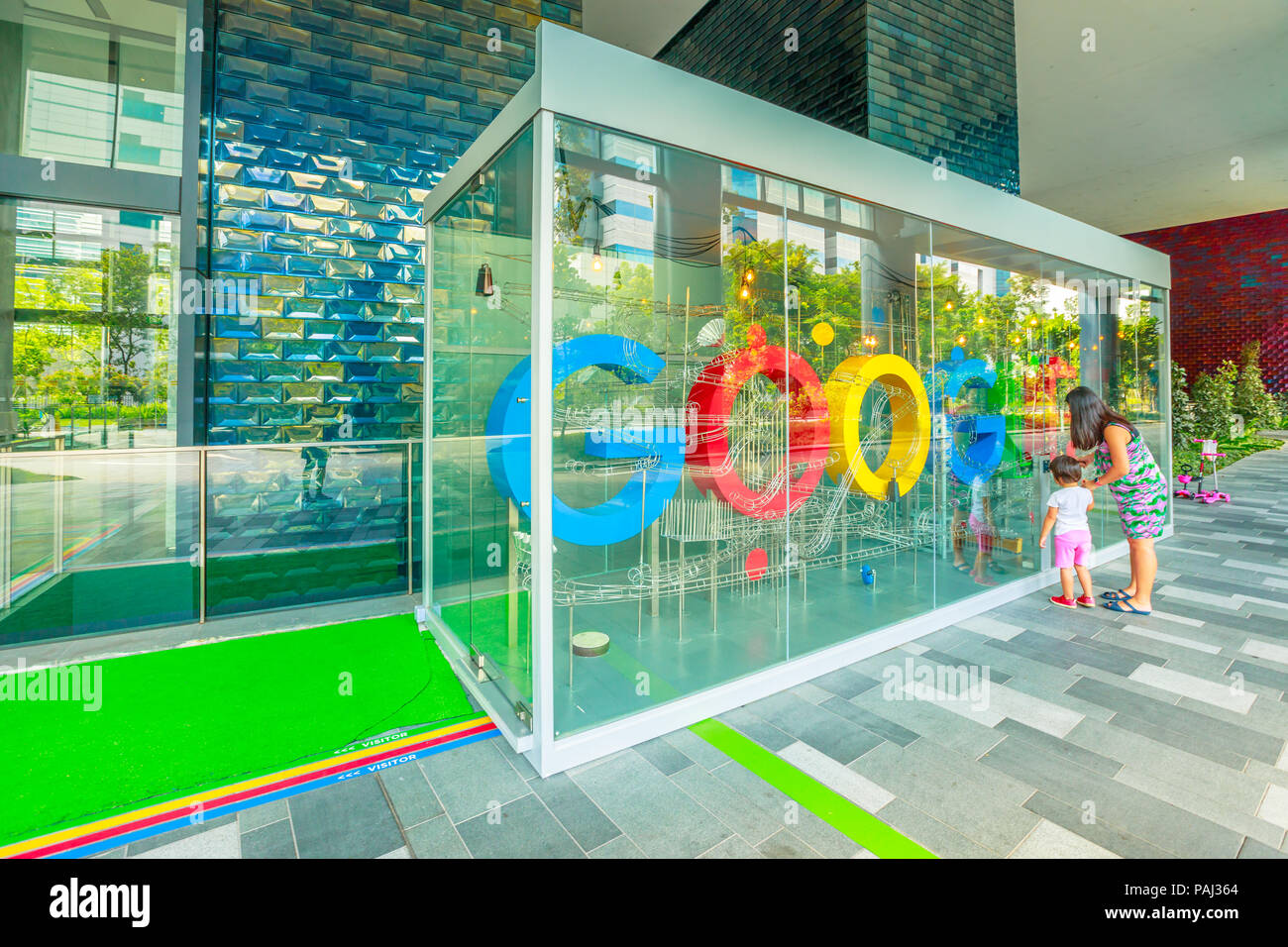 Singapore - Maggio 5, 2018: Google Sign on lobby of new Google Headquarters, Mapletree Business City II in Singapore, Asia. Little girl with mom turn to funny wheel that chimes music. Stock Photo