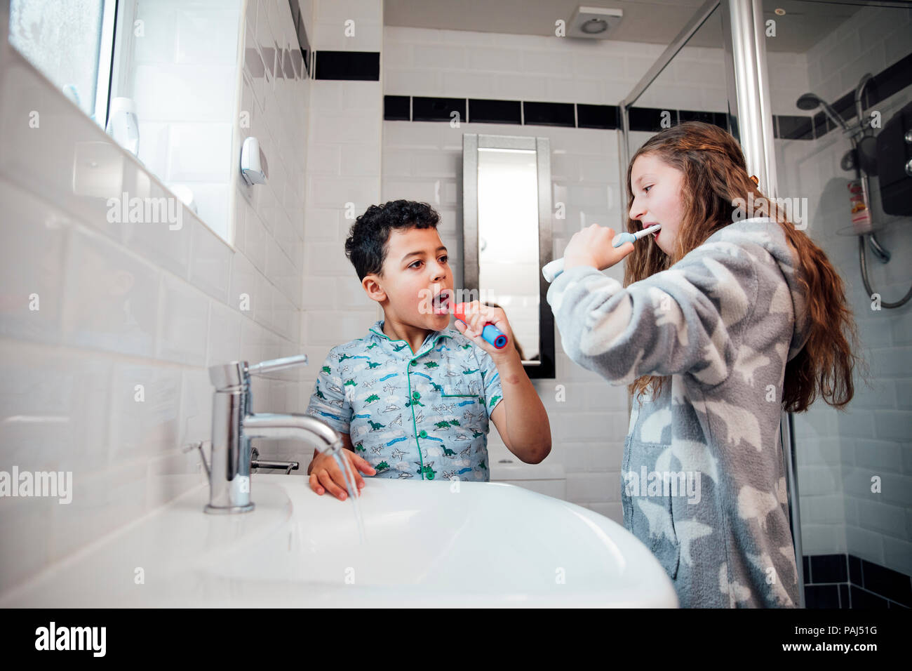 Little boy and his older sister are brushing their teeth together in the bathroom at home. Stock Photo