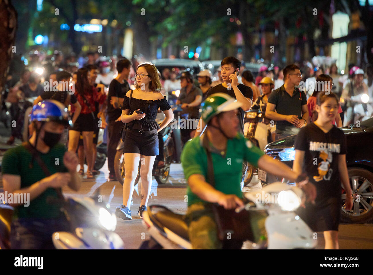 Night shot of pedestrians crossing road full of mopeds in busy