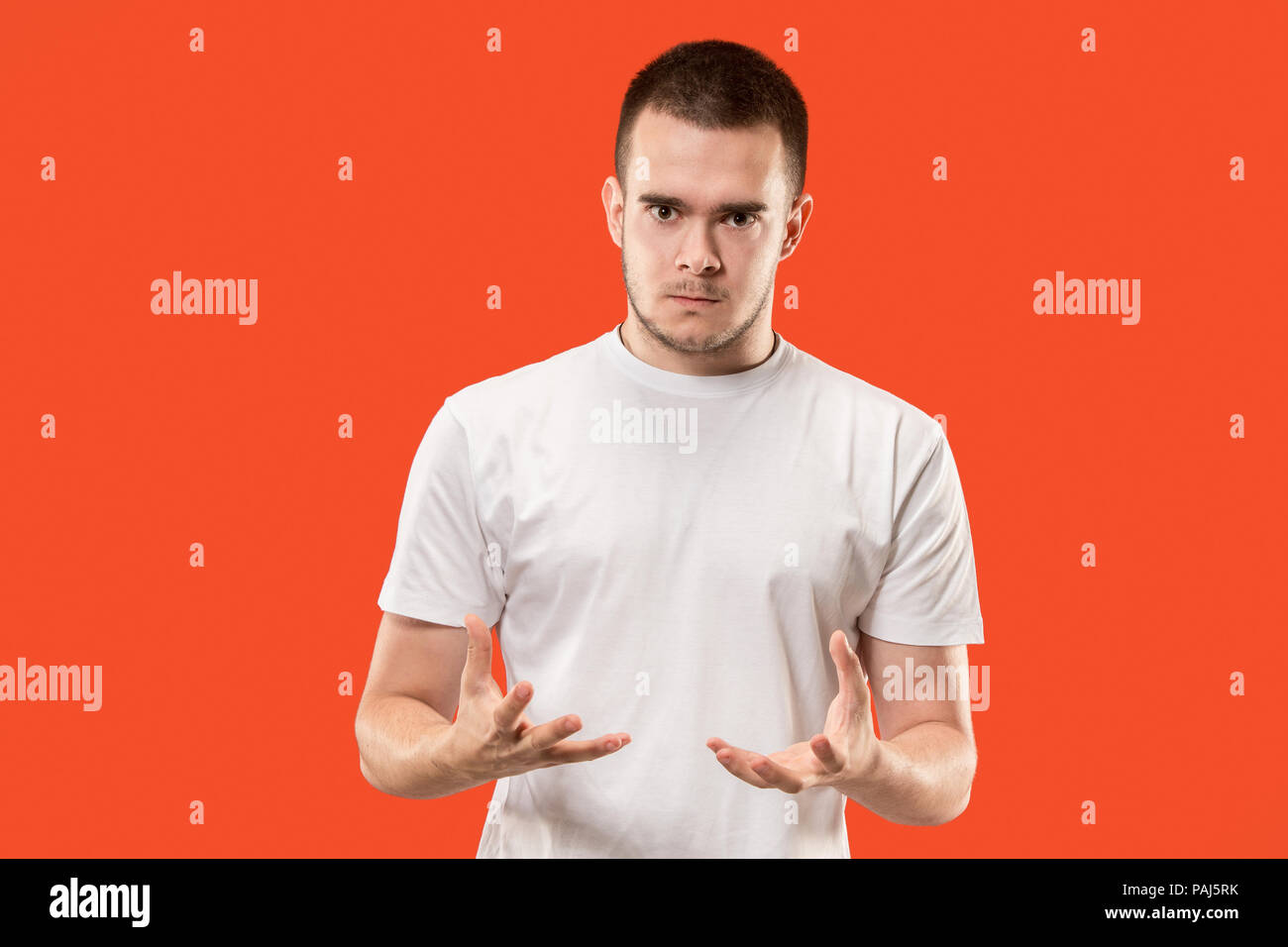 The young emotional angry man on orange studio background Stock Photo