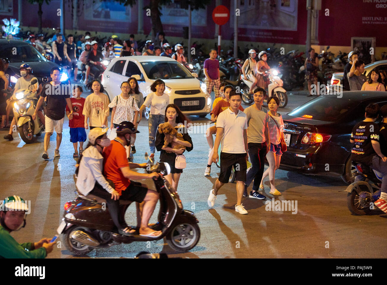 Night shot of pedestrians crossing road full of mopeds in busy