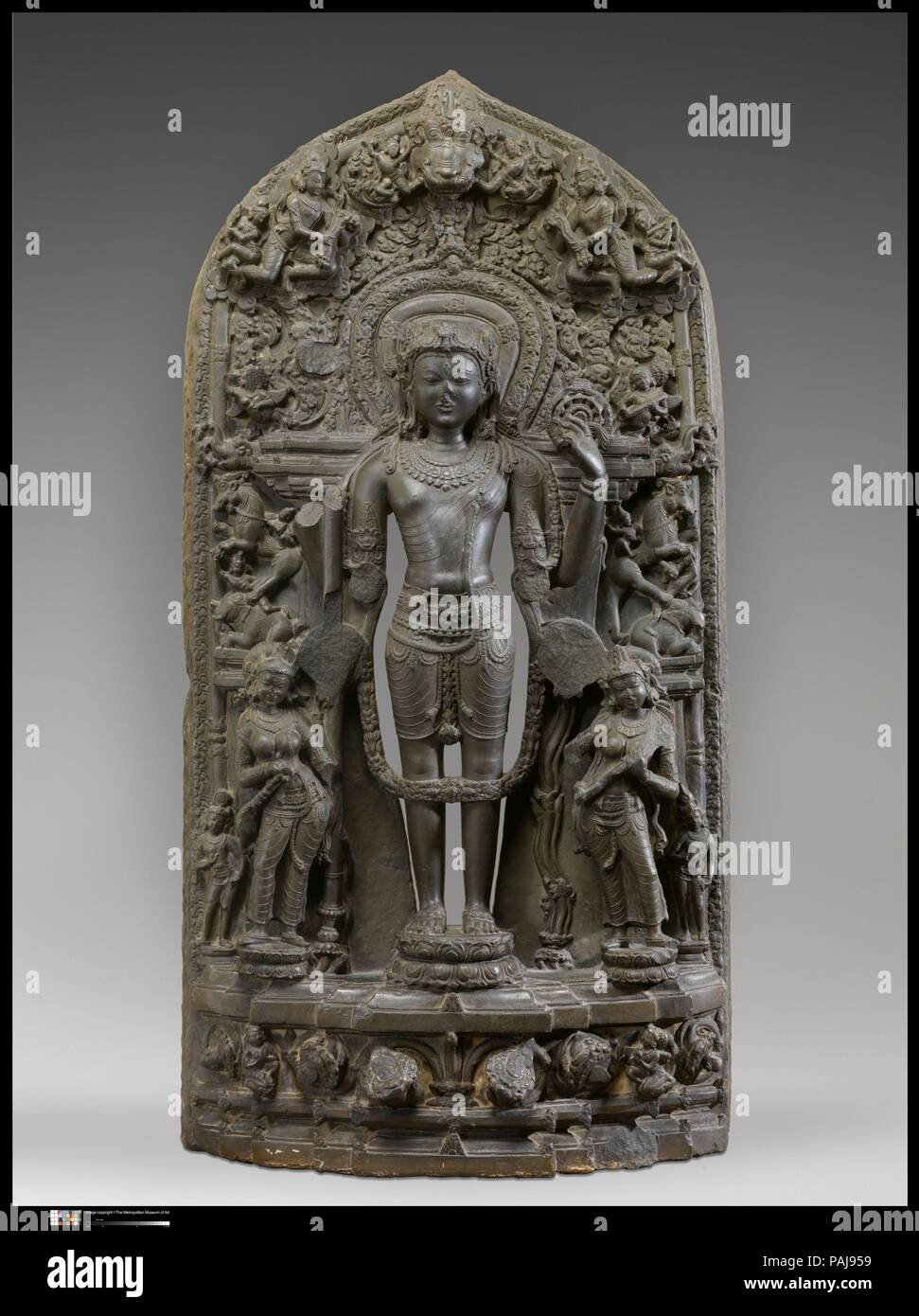 Vishnu Accompanied by Lakshmi and Sarasvati. Culture: Bangladesh. Dimensions: H. 47 in. (119.4 cm); W. 25 in. (63.5 cm); D. 9 in. (22.9 cm). Date: 12th century.  Vishnu stands in perfect symmetry (samapada), the protector of cosmic order. In an iconographic convention unique to medieval Bengal, he is accompanied by the goddesses Lakshmi, holding a fly-whisk (camara) and lotus (padma), and Sarasvati, playing a vina, rather than by his wives Sri Devi and Bhu Devi. He is also closely associated with Priti, the earth goddess, who often appears between his feet. The goddesses in turn are flanked by Stock Photo