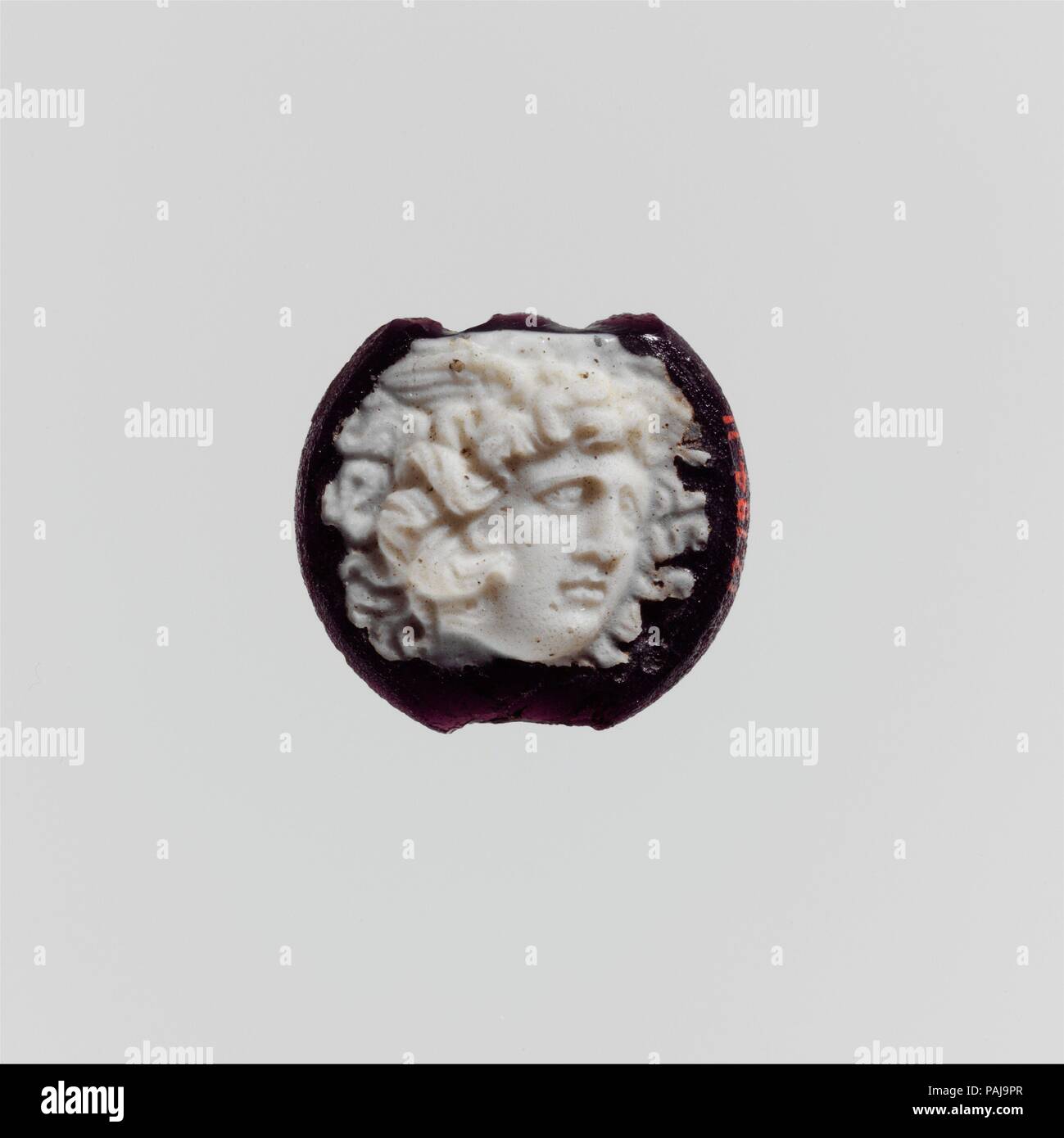Cameo glass disk with Medusa head. Culture: Roman. Dimensions: Overall: 7/8 x 1 in. (2.2 x 2.5 cm). Date: 1st century A.D..  Translucent deep purple with opaque white overlay.  Circular disk, with beveled edge; flat back.  On front, in deep relief in white, head of Medusa in three-quarter view to right, with wings and serpents in her hair.  Broken and chipped at top and bottom; dulling and faint iridescent weathering. Museum: Metropolitan Museum of Art, New York, USA. Stock Photo
