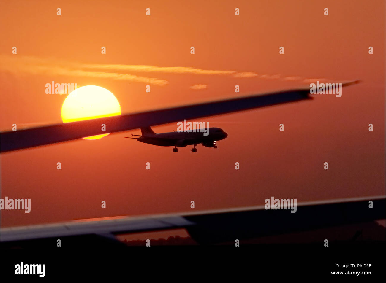 A320 landing at sunset past the horizontal-stabiliser of an A330 at sunset Stock Photo