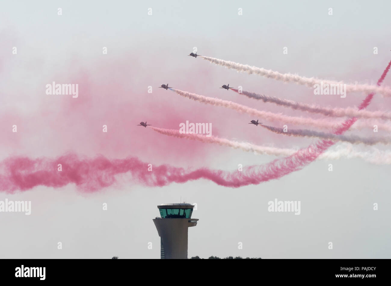 Red Arrows in the flying-display with red and white smoke with the air-traffic control-tower behind at the 2006 Farnborough International Airshow Stock Photo