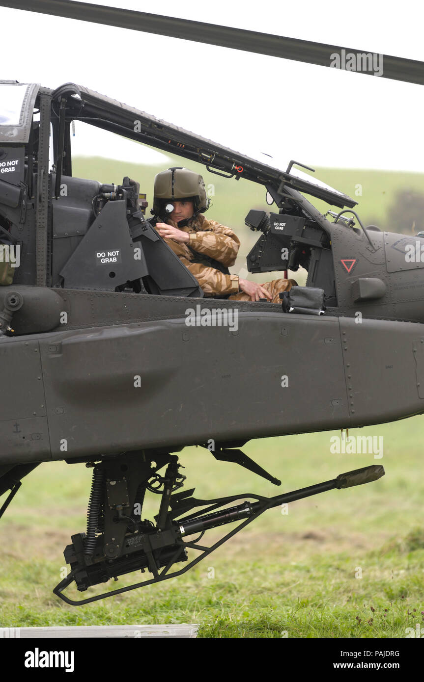 pilot wearing helmet in the cockpit of a British Army Air Corps Boeing WAH-64D Apache AH-1 with 30 millimetre chain-gun parked on the grass at the Bri Stock Photo