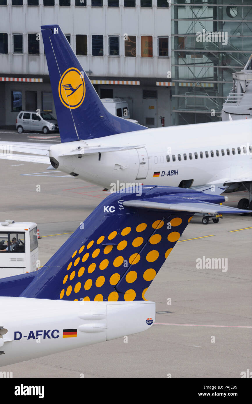 tail-fins of Contact Air Interregional Fokker 100 taxiing and Lufthansa Boeing 737 parked at the terminal behind Stock Photo