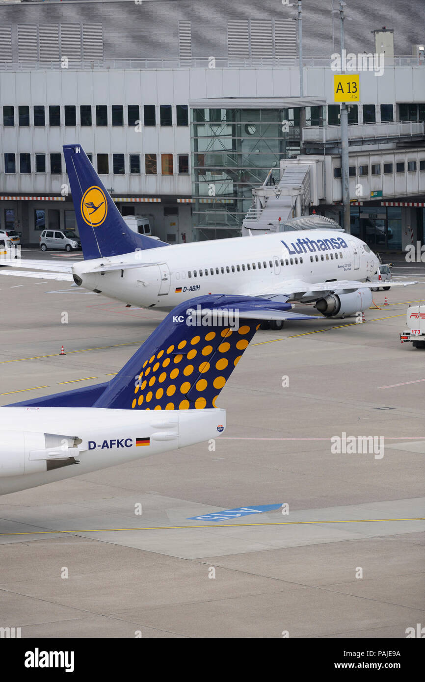 tail-fin of Contact Air Interregional Fokker 100 taxiing and Lufthansa Boeing 737 parked at the terminal behind Stock Photo