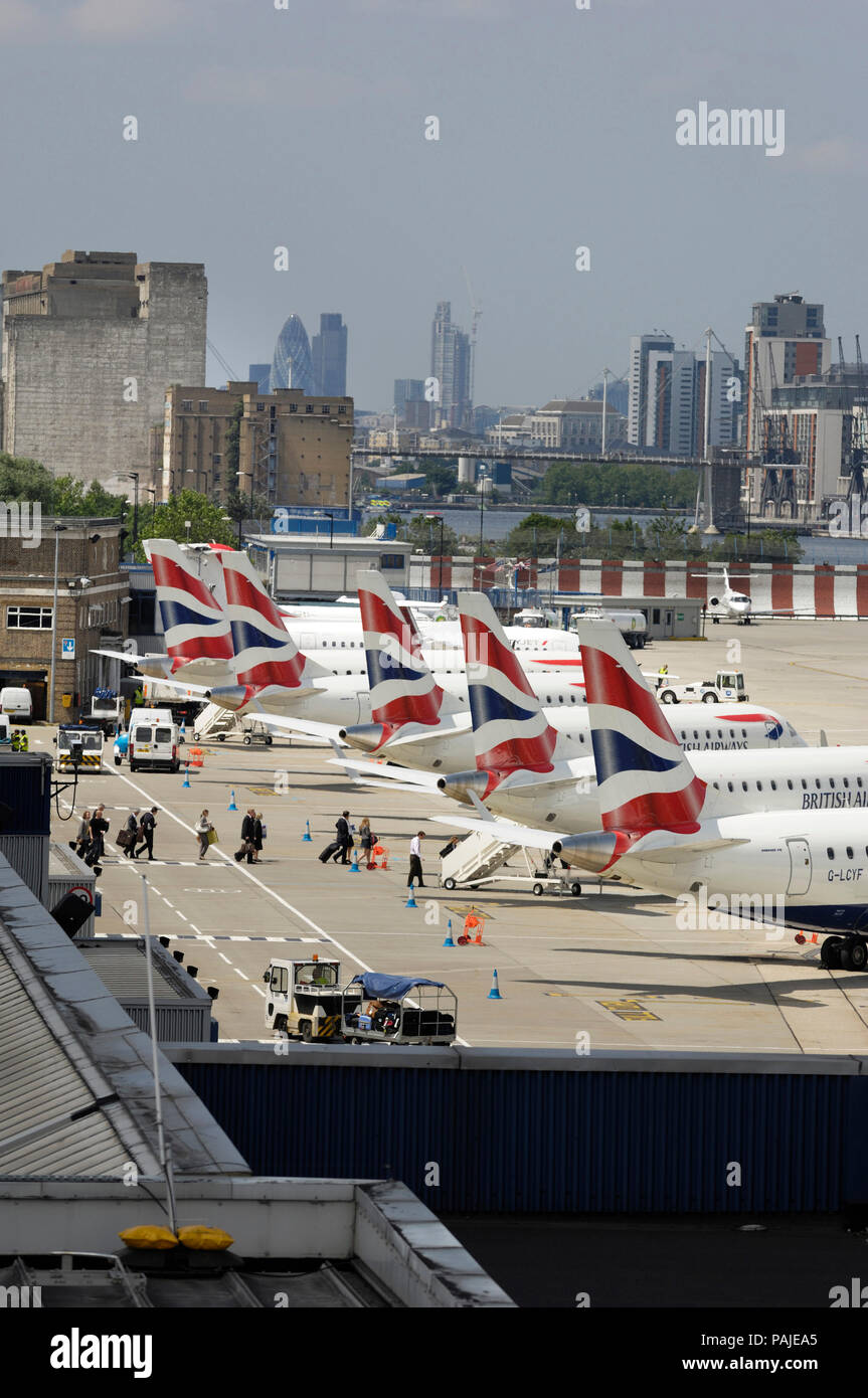 tail-fins of British Airways BA CityFlyer Embraer 170s parked in a row at London City with skyscrapers behind Stock Photo
