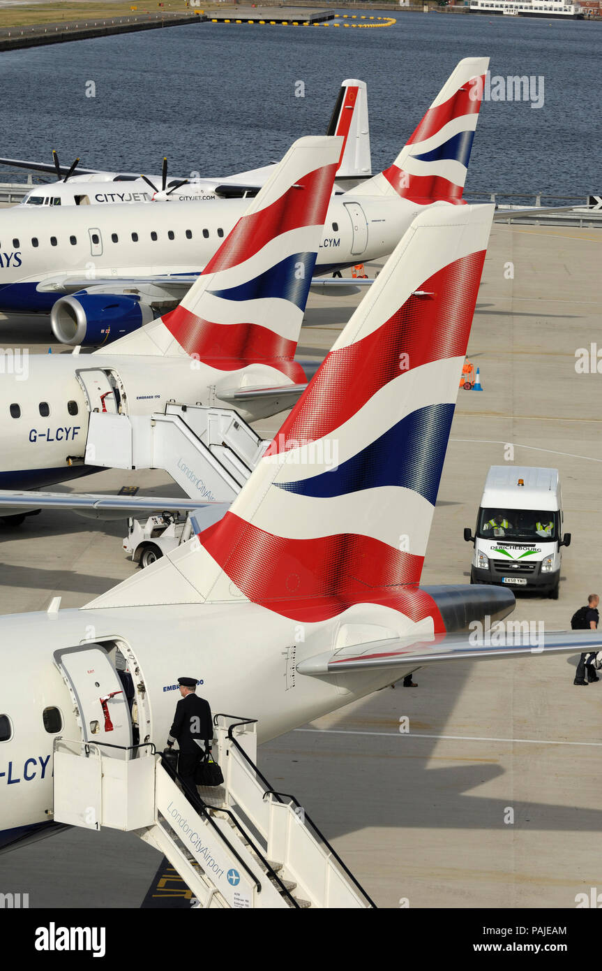 tail-fins of British Airways BA CityFlyer Embraer 170, 190s and CityJet Fokker F-50 parked in a row at London City Stock Photo
