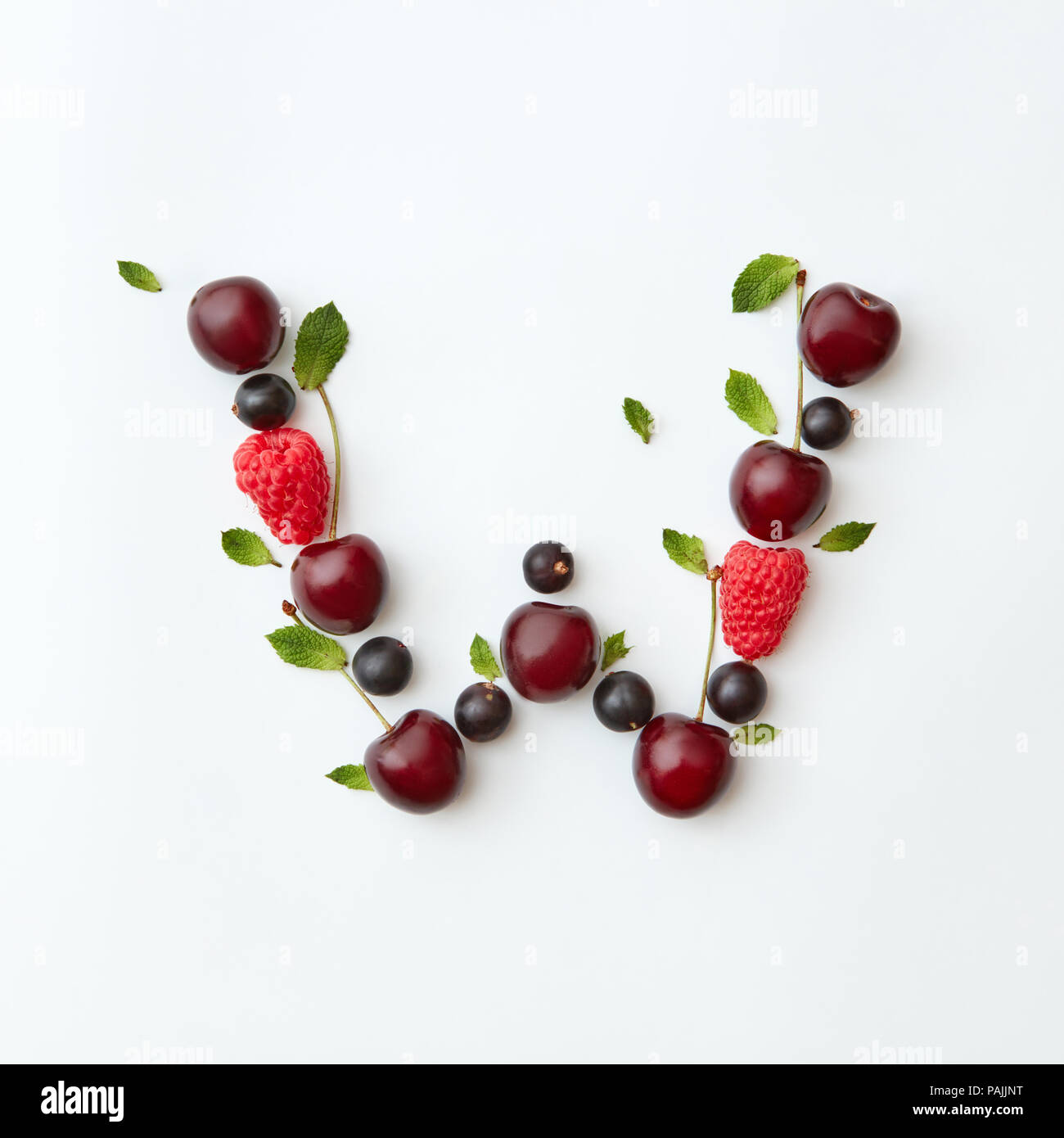 Summer berries pattern of letter W english alphabet from natural ripe berries - black currant, cherries, raspberry, mint leaf isolated on a white background. Stock Photo