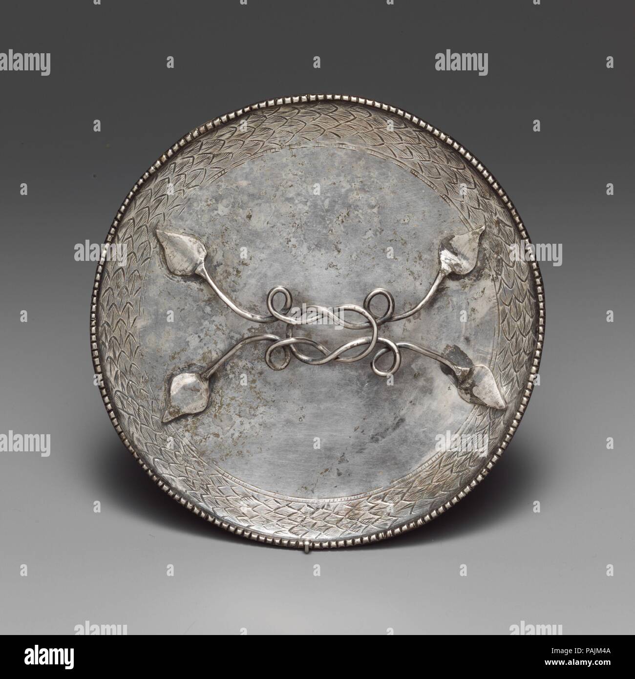 Silver mirror. Culture: Roman. Dimensions: Diam.: 5 3/16 in. (13.2 cm). Date: 4th century A.D..  The type of mirror with a horizontal handle originated in the Roman world during the first century B.C. It  was subsequently adopted in various cultures of Asia and finally died out in the ninth to tenth century A.D. In this example, the classical origins are clear in the leaf-shaped attachments of the handle, the Herakles knot, and the wreath around the circumference of the disk. Museum: Metropolitan Museum of Art, New York, USA. Stock Photo