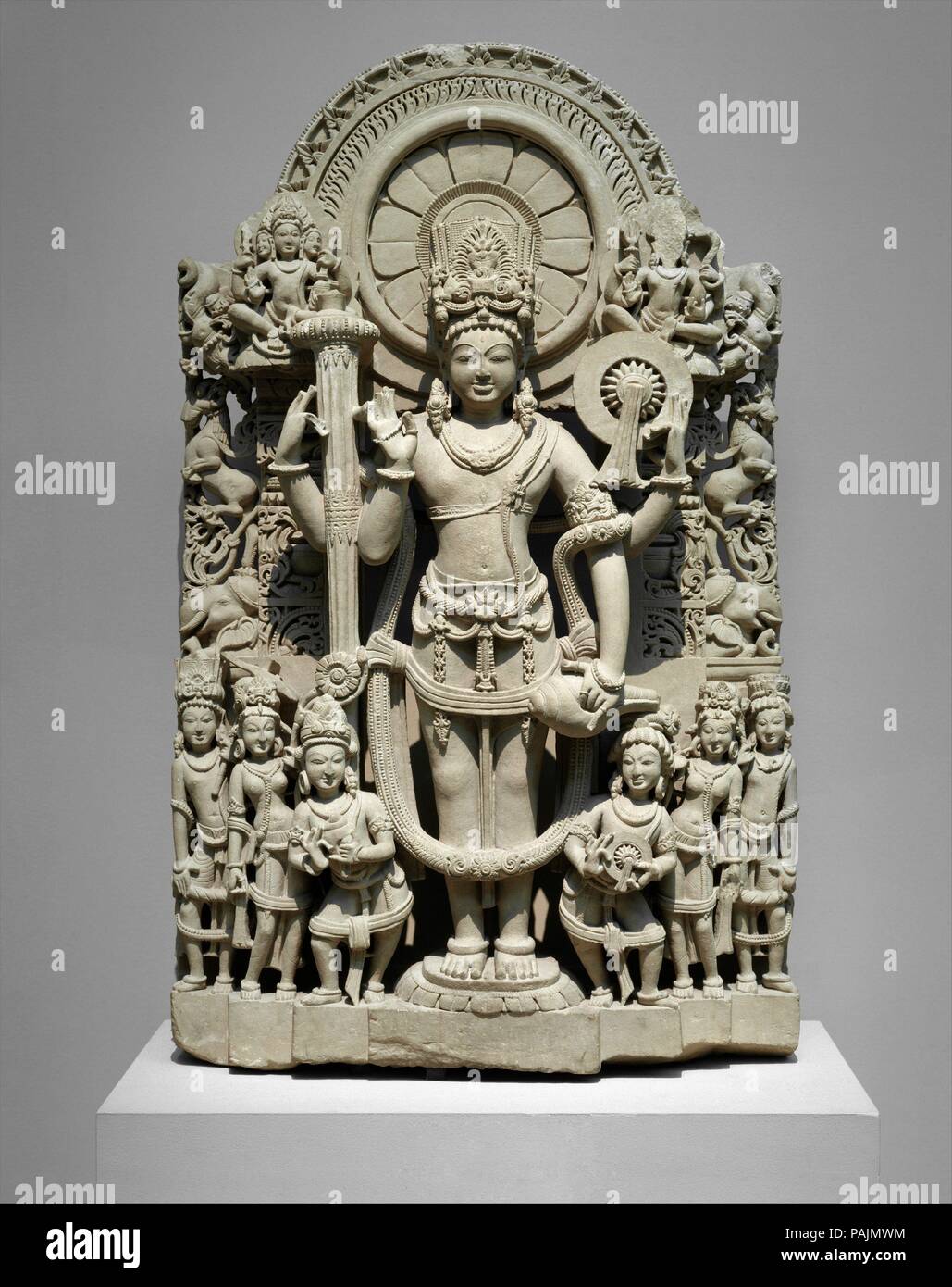 Vishnu. Culture: India (Punjab). Dimensions: H. 43 1/2 in. (110.5 cm); W. 25 5/8 in. (65.1 cm); D. 10 in. (25.4 cm). Date: 10th-11th century.  This elaborate stela of the god Vishnu shows him at the center holding his usual attributes (clockwise from upper right): a chakra (war discus), a conch-shell trumpet, and a gada (mace). His raised hand is held in abhayamudra, or the fear-allaying gesture. He wears a tall miter and a long garland of flowers. His head is surrounded by an ornate nimbus with bands of lotus petals, flames, and abstracted triangular floral motifs. Flanking his legs are six f Stock Photo