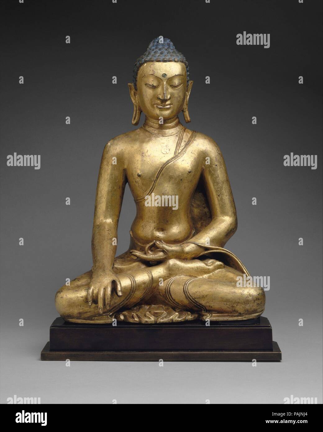 Buddha Shakyamuni or Akshobhya, the Buddha of the East. Culture: Tibet. Dimensions: H. 22 3/4 in. (58 cm). Date: 11th-12th century.  The robust body of this early Tibetan Buddha seems to derive from the art of the North Indian post-Gupta period (seventh to eighth century), while its physiognomy is based on Central Asian prototypes of similar date. Few works of art from tenth-century Tibet have survived, but what does remain seems to be an eclectic synthesis of elements drawn from the artistic traditions of Central Asia, India, Nepal, and China.  The identification of the statue is difficult. T Stock Photo