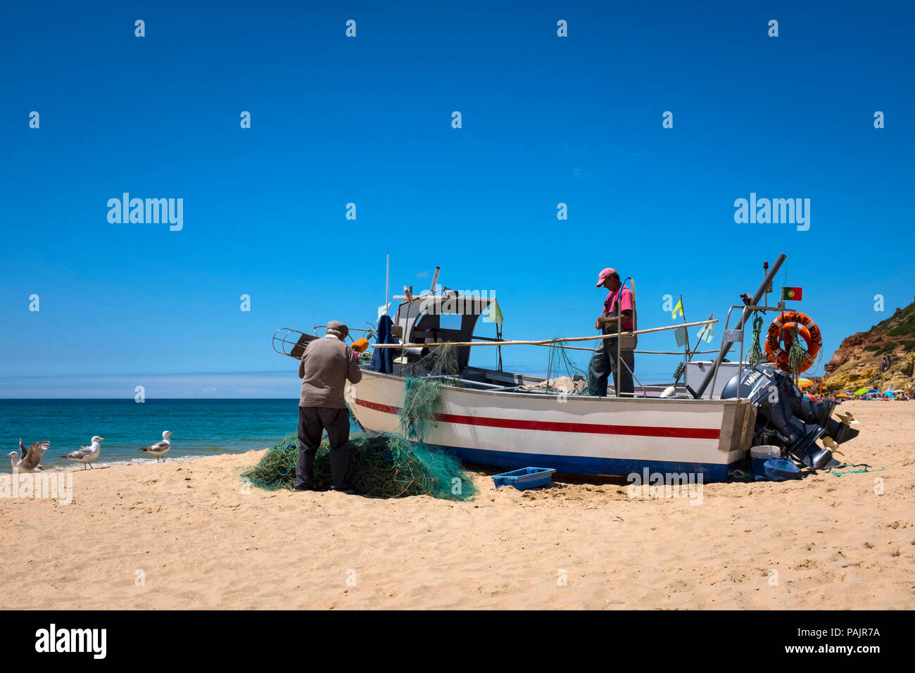 Small-scale fishermen cleaning their nets, in Salema, Algarve, Portugal. Stock Photo