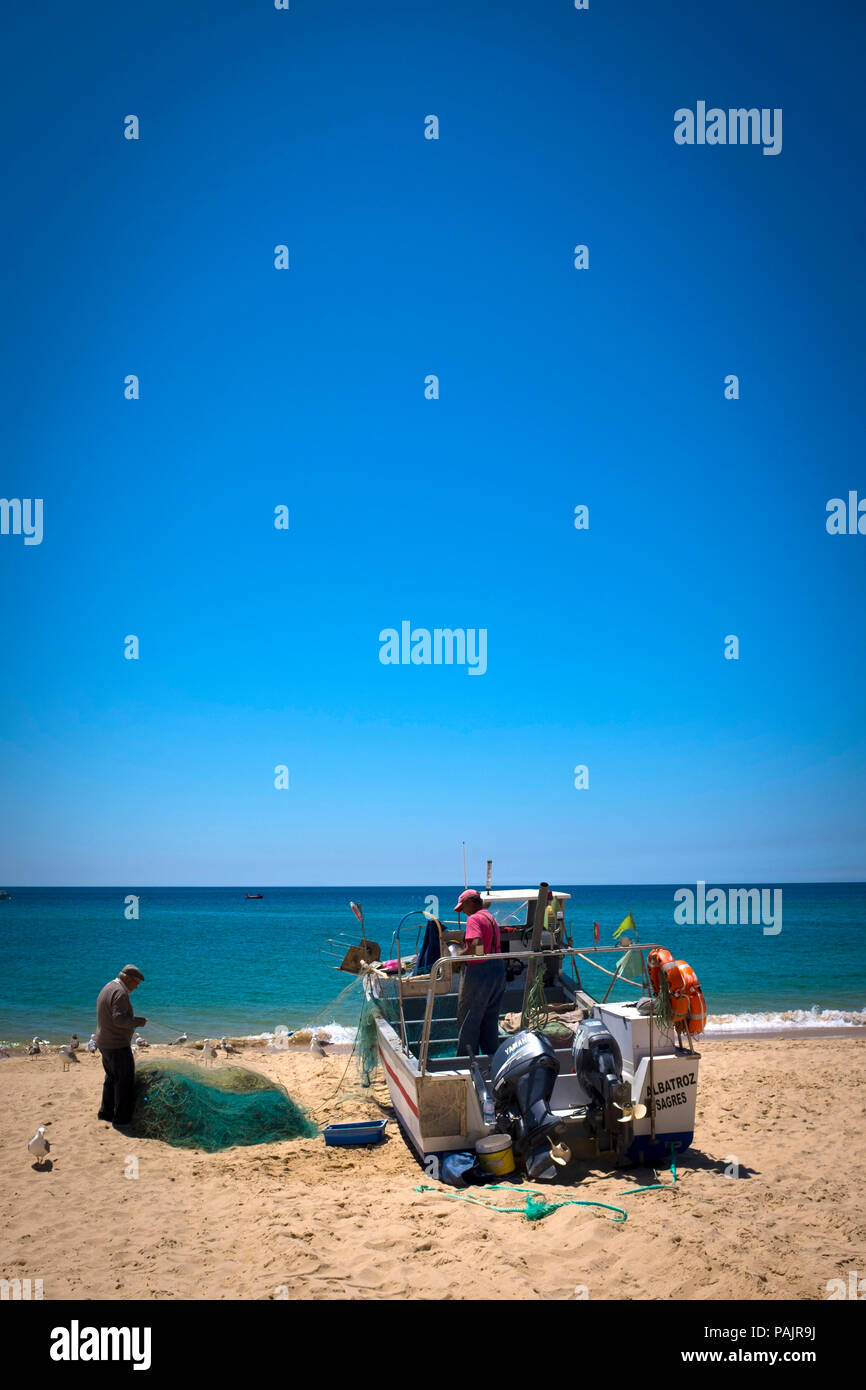 Small-scale fishermen cleaning their nets, in Salema, Algarve, Portugal. Stock Photo