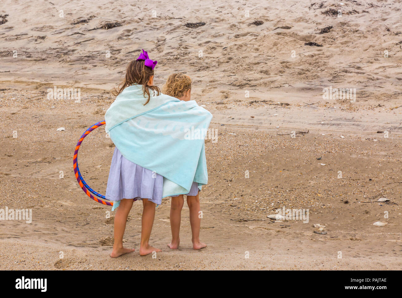 two young girls at the beach sharing a towel and looking away from the camera Stock Photo