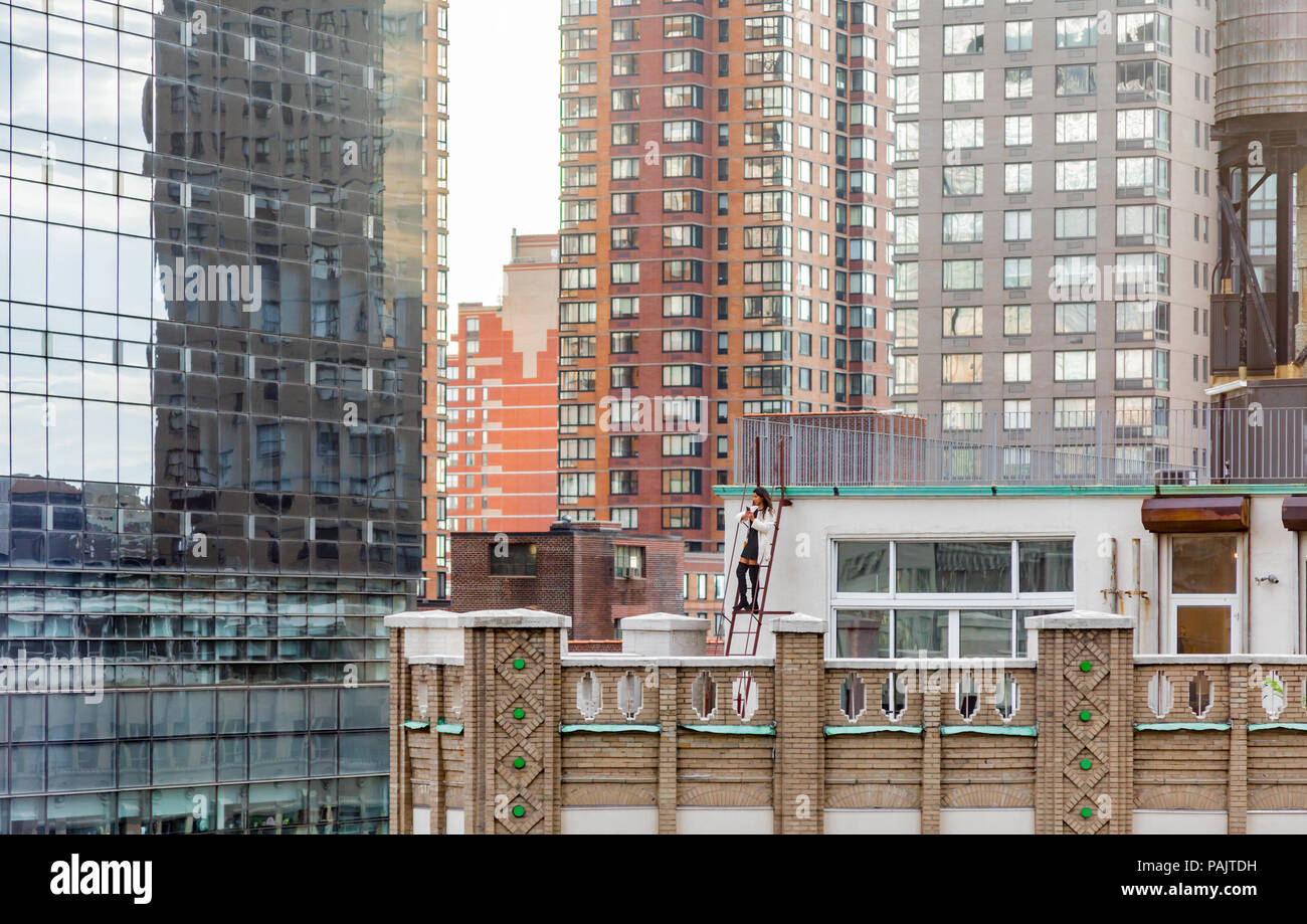 well dressed woman standing on a ladder on the roof of a NYC building taking pictures Stock Photo