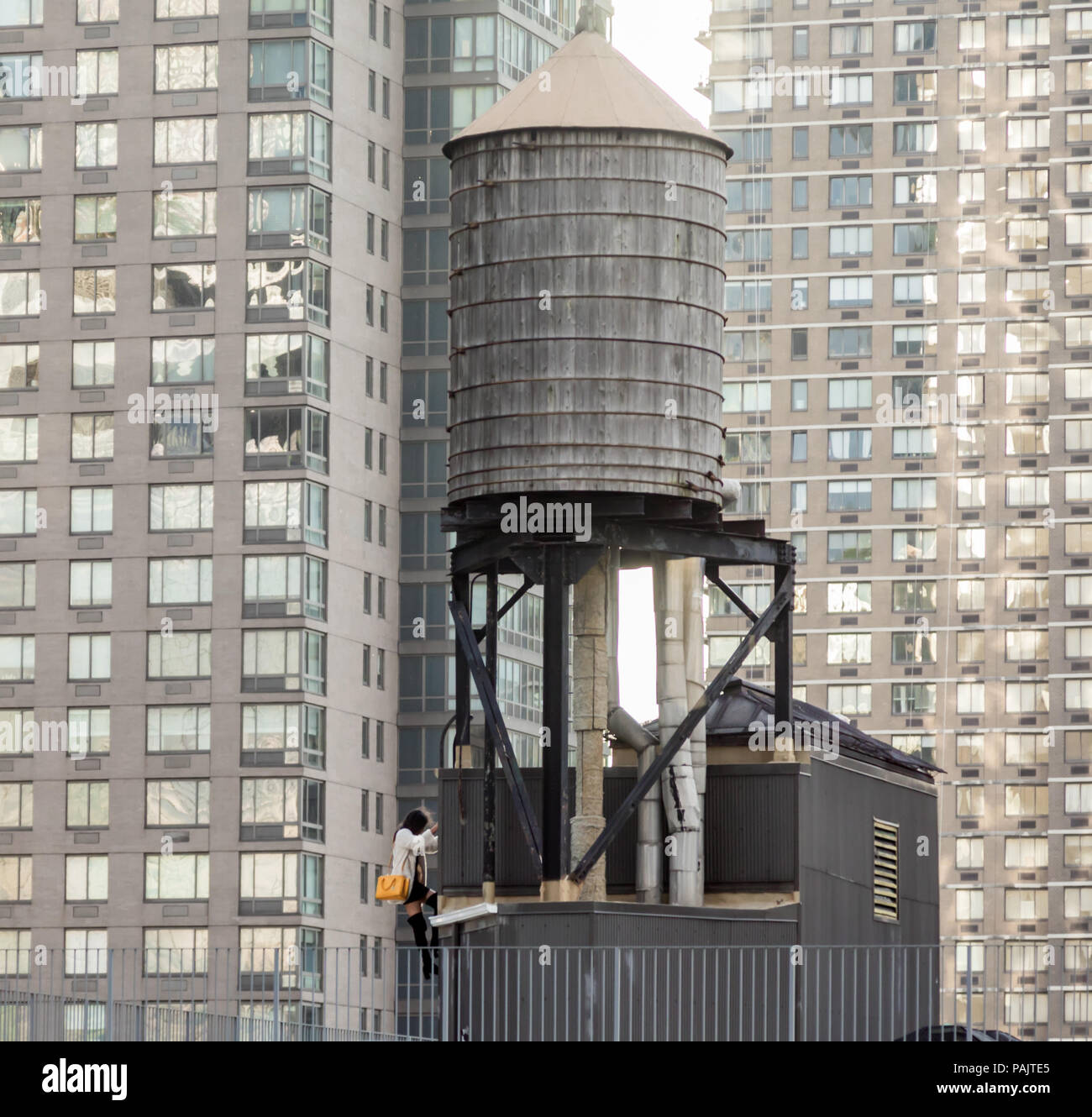 well dressed young woman climbing the ladder of a water tower on the roof of a NYC building Stock Photo