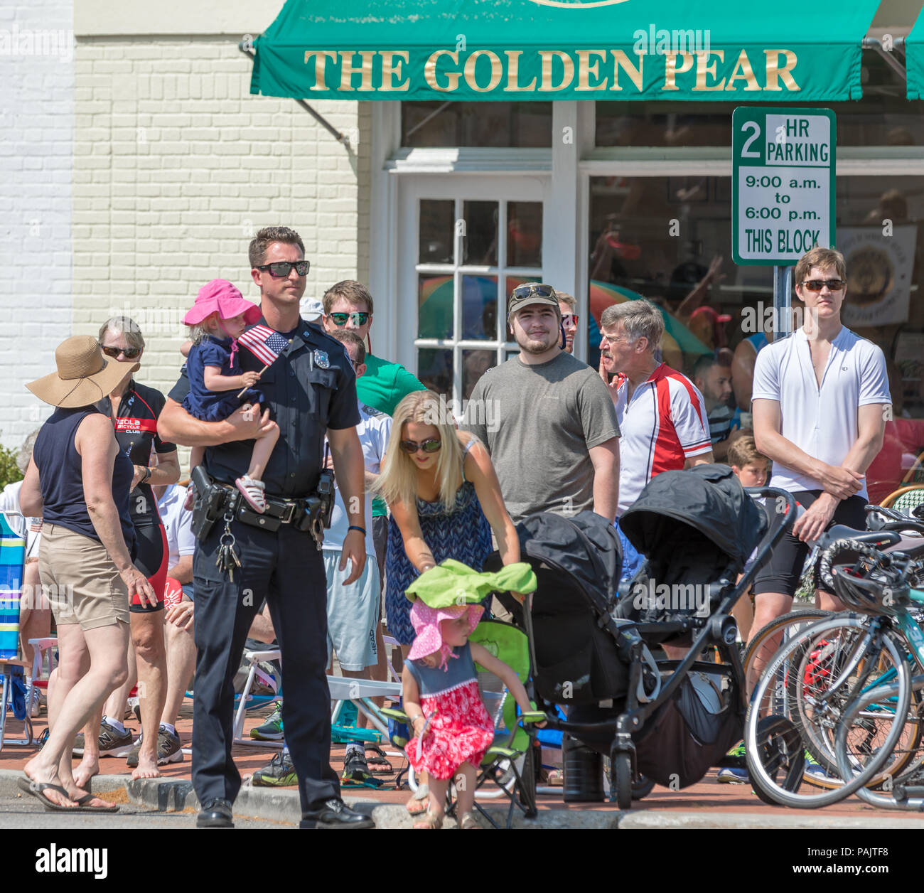police officer holding a baby and other people awaiting the start of a fourth of July parade in Southampton, NY Stock Photo