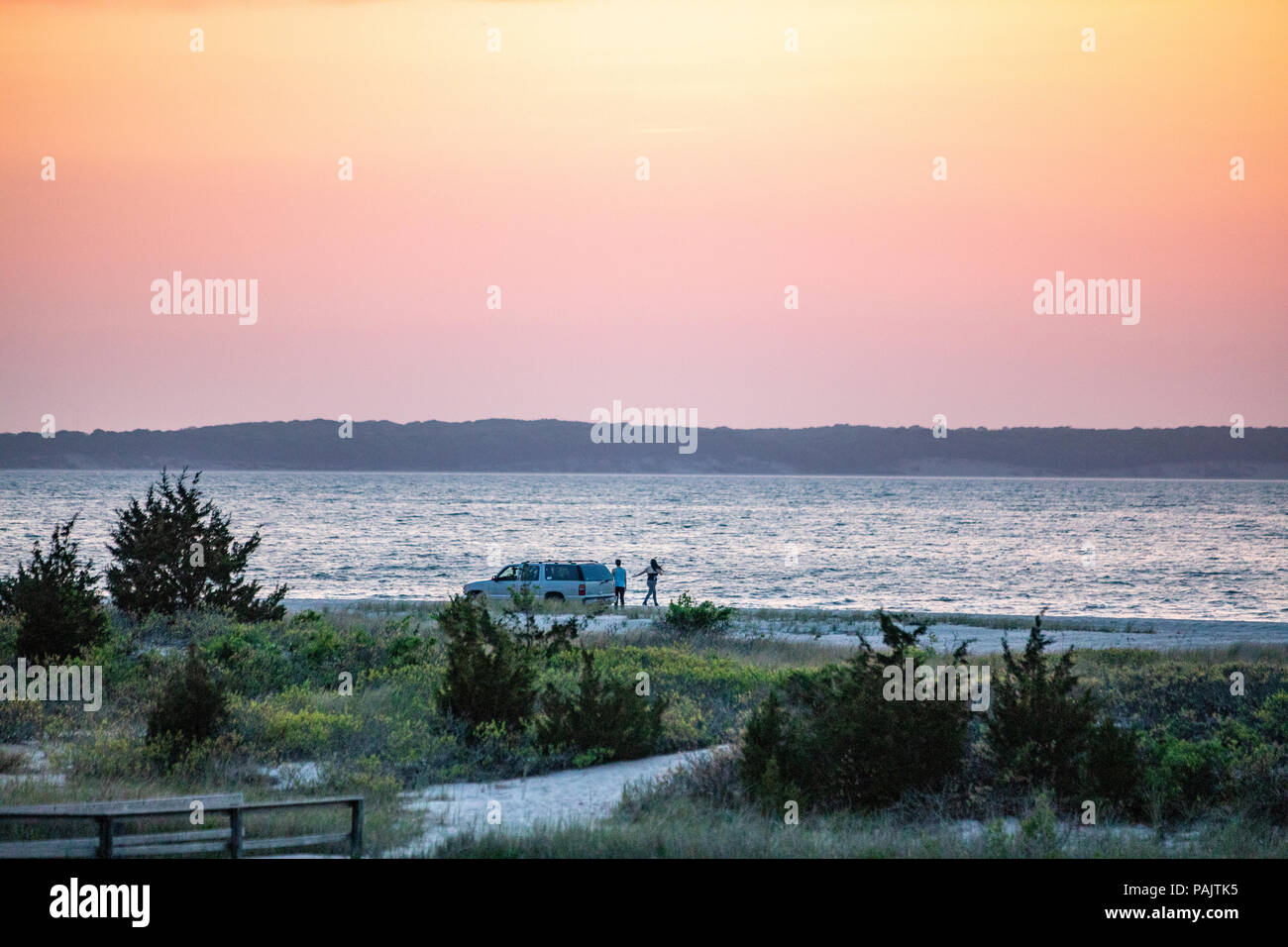two people and a white four wheel drive truck on a beach at sunset Stock Photo