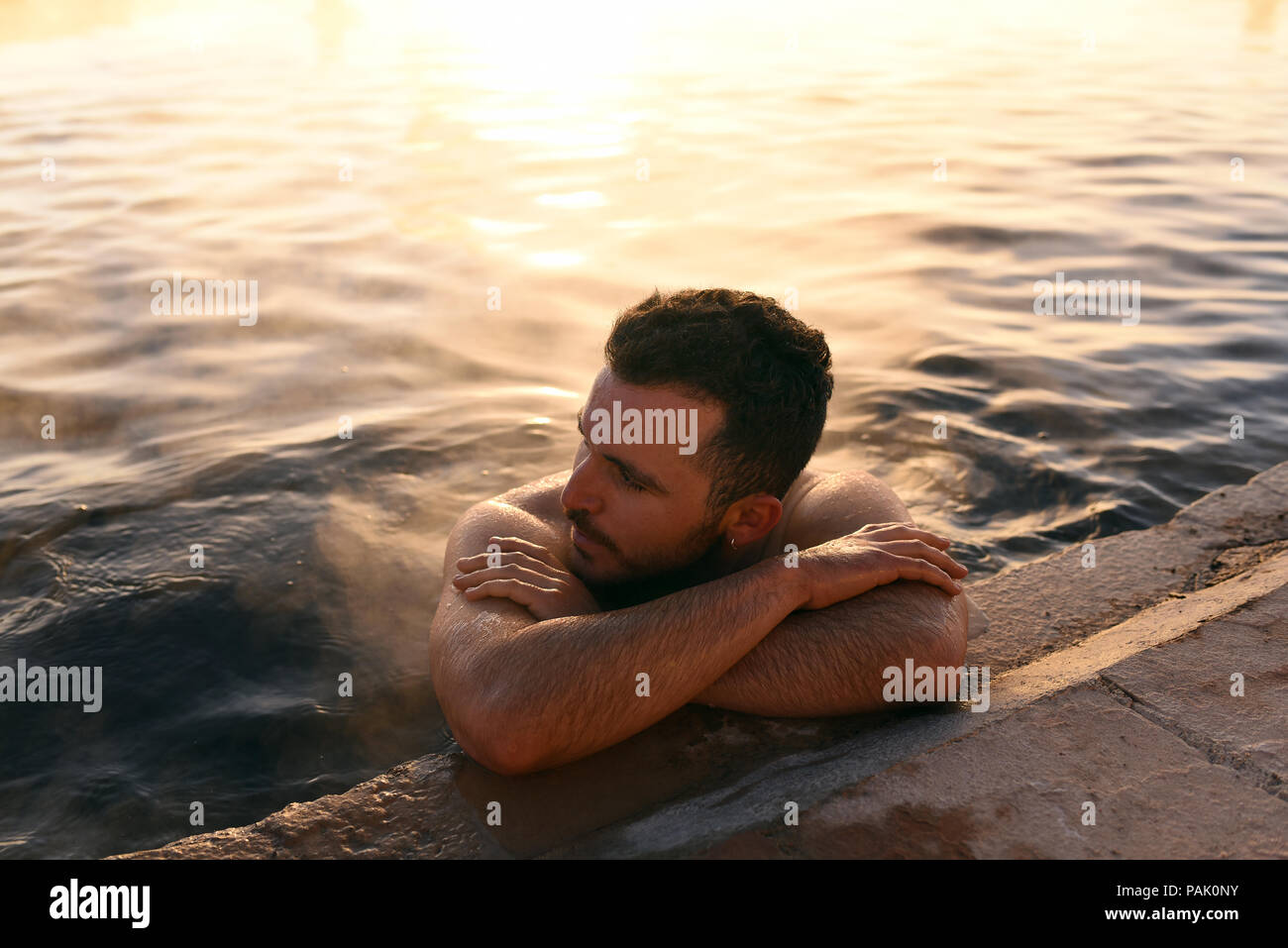 Man bathing in the hot springs with sunrise lit steam rising in the background. Termas de Polques, Sud Lípez province, Bolivia. Stock Photo