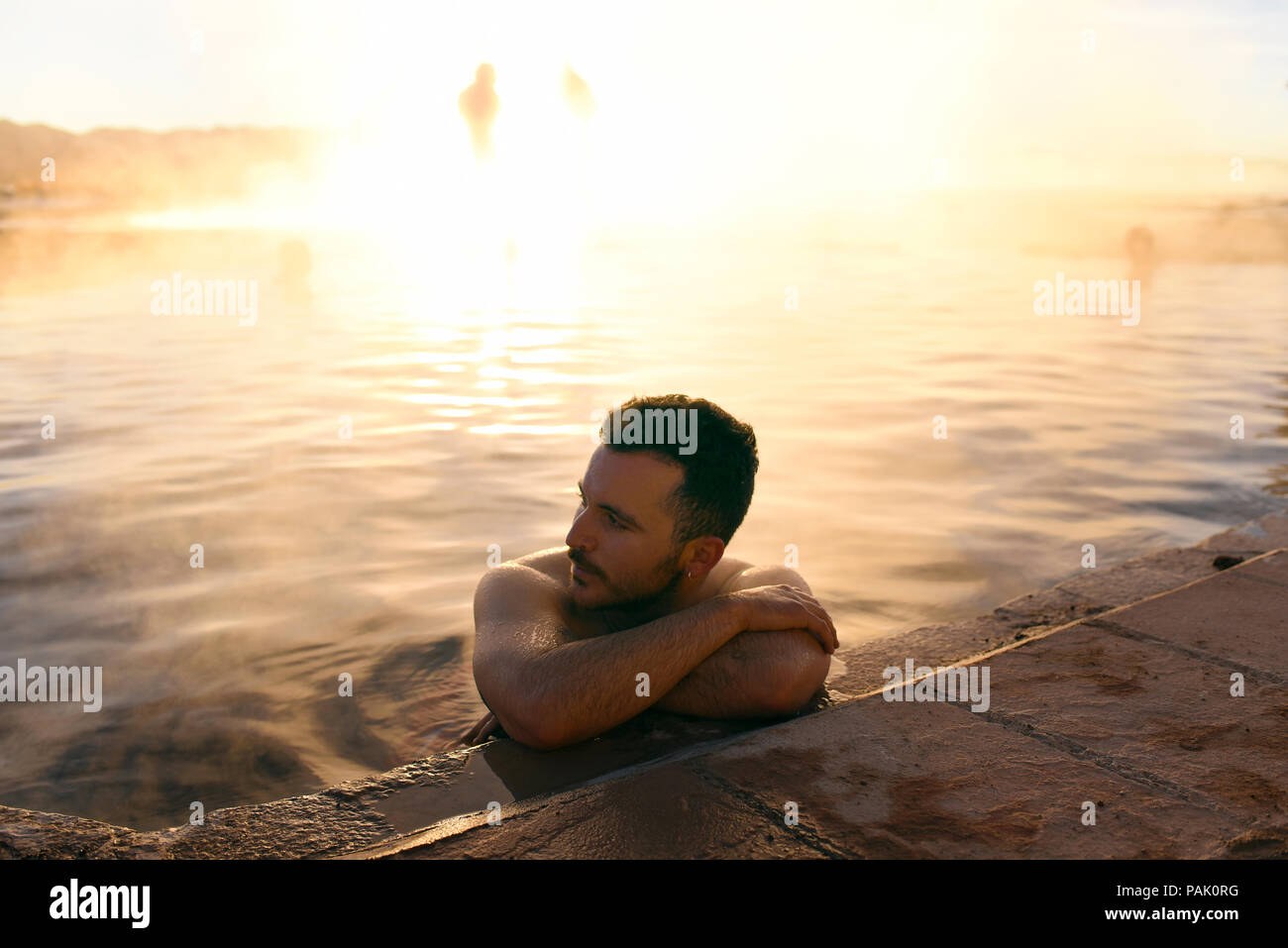Man bathing in the hot springs, with sunrise lit steam rising in the background. Termas de Polques, Sud Lípez province, Bolivia. Stock Photo