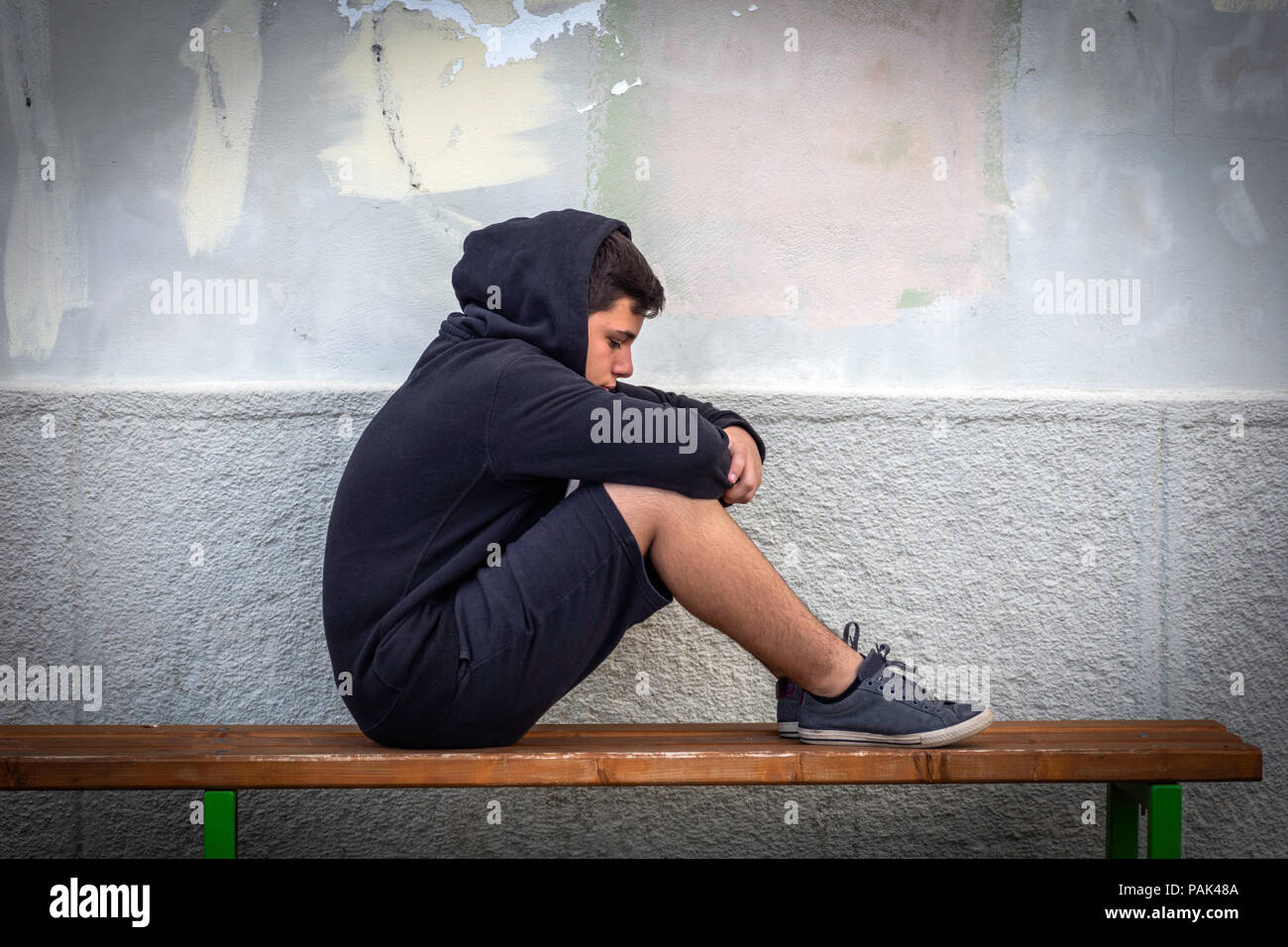 Little boy sad sitting alone at school hides his face Stock Photo