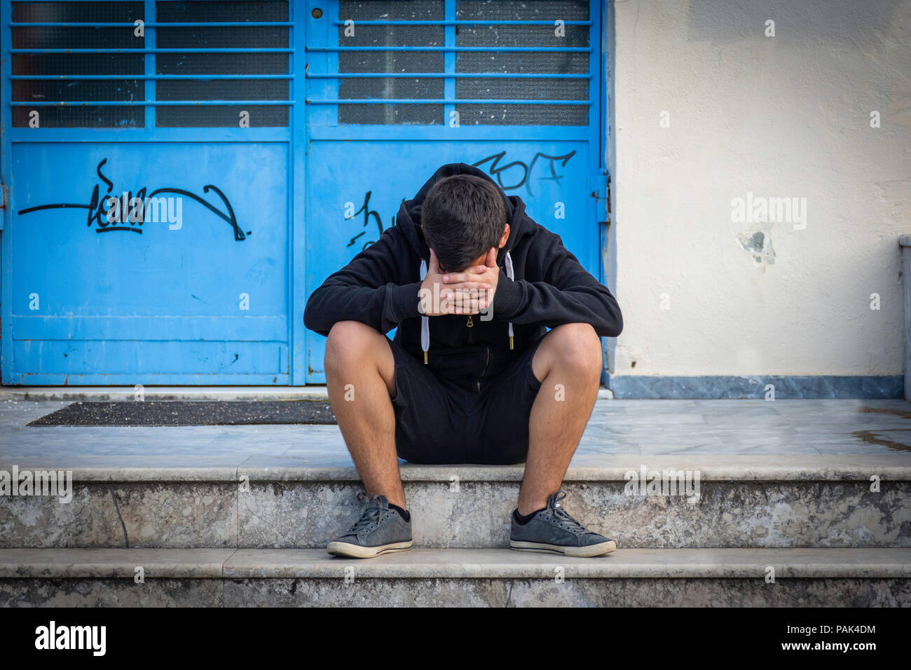 Little boy sad sitting alone at school hides his face Stock Photo