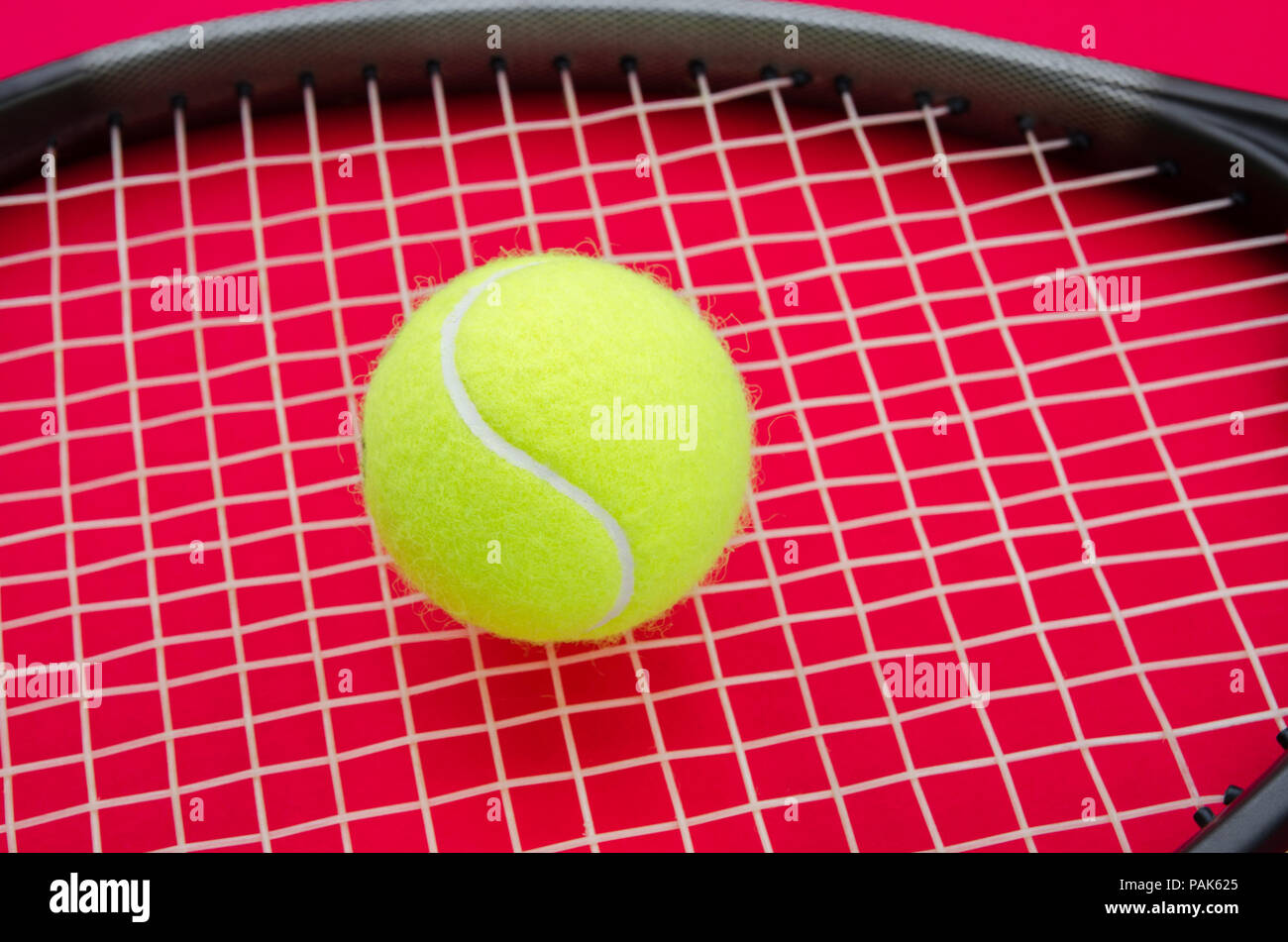 Tennis ball on a raquet with a red alerted serious background suggesting an important match set game or point in this great elegant sport Stock Photo