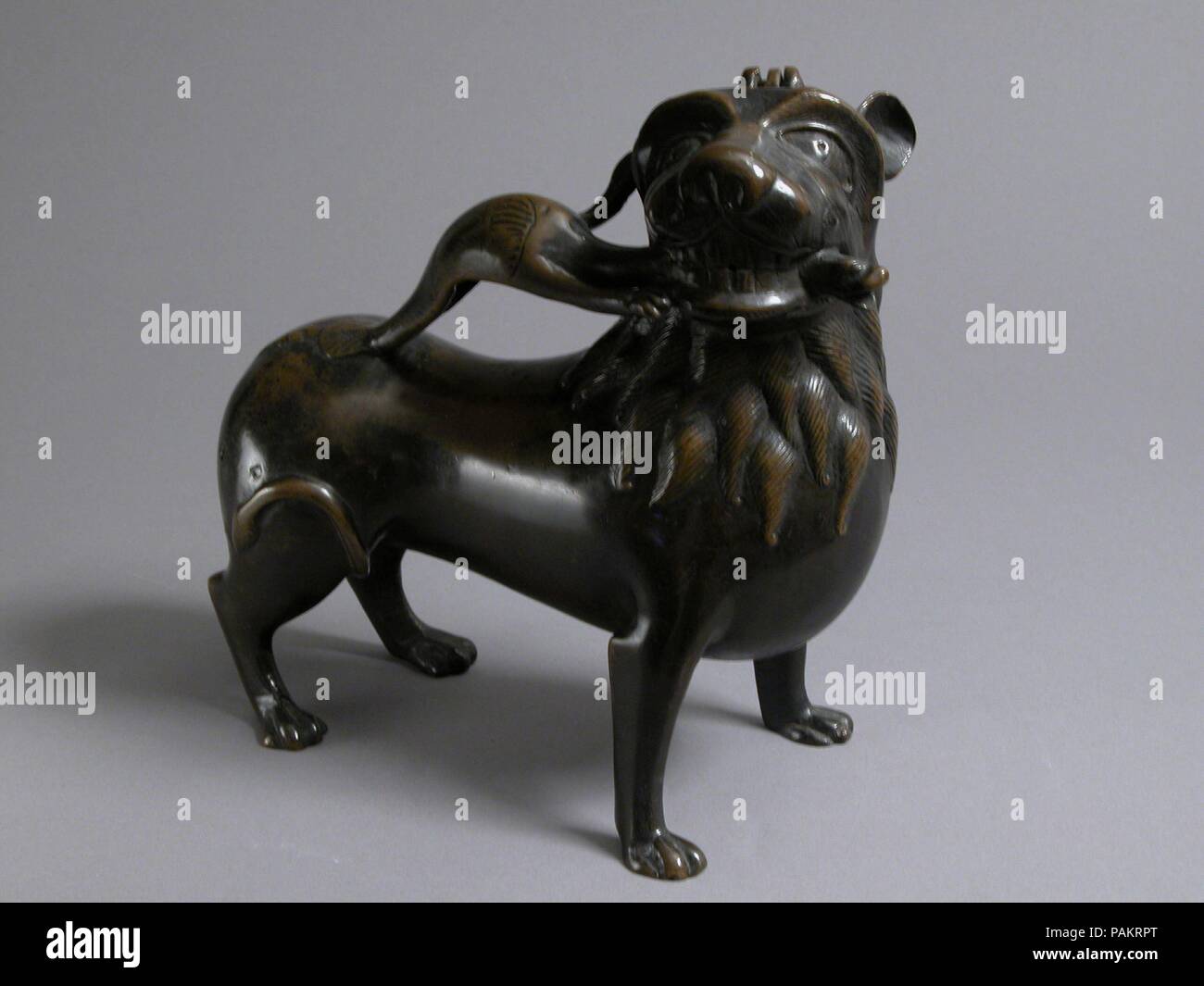 Aquamanile in the Form of a Lion. Culture: North German. Dimensions: Overall: 9 1/8 x 8 15/16 x 3 3/4 in. (23.2 x 22.7 x 9.5 cm)  Thickness PD: 3/50-1/10 in. (0.15-0.25 cm)  Weight PD: 84.3oz. (2391g). Date: ca. 1200.  This aquamanile is distinguished by the lion's turned head, which grasps the neck of the dragon in its jaws. The dragon here serves as both handle and spout. Museum: Metropolitan Museum of Art, New York, USA. Stock Photo
