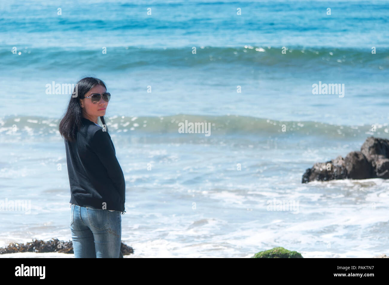 A chinese woman near the waves and pacific ocean at El Matador Beach in California on a sunny cloudless sky day. Stock Photo