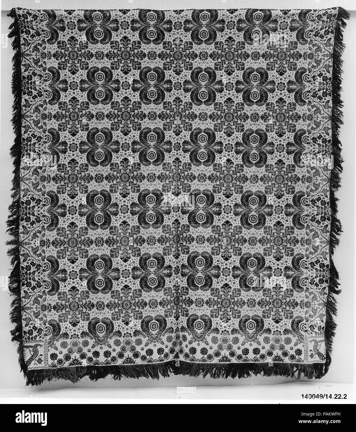 Coverlet. Culture: American. Dimensions: 98 1/2 x 89 3/4 in. (250.2 x 228 cm). Date: ca. 1840.  This coverlet is woven in two panels and seamed at the center. It has a warp of undyed and light blue cotton and a weft of dark blue, green, and red wool and undyed cotton. The central field shows feather medallions alternating with foliate medallions. The bottom border has a stylized vine motif, and the right and left borders have roses and tulips. Peacocks adorn each of the two corner blocks. Both sides of the coverlet have natural fringe, and there is attached fringe along the bottom edge. Museum Stock Photo